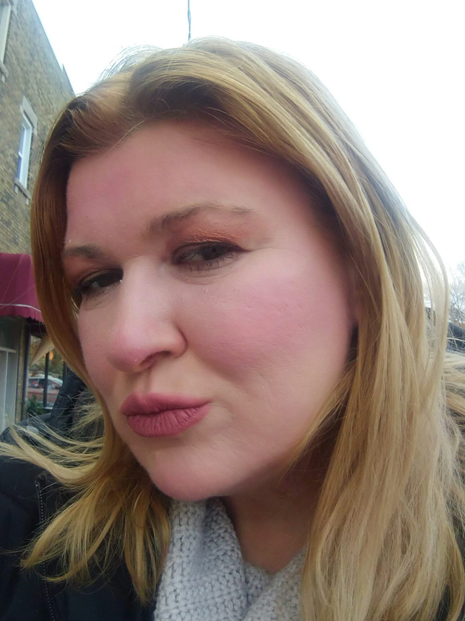 Close-up of a woman with blonde hair making a playful facial expression outdoors.