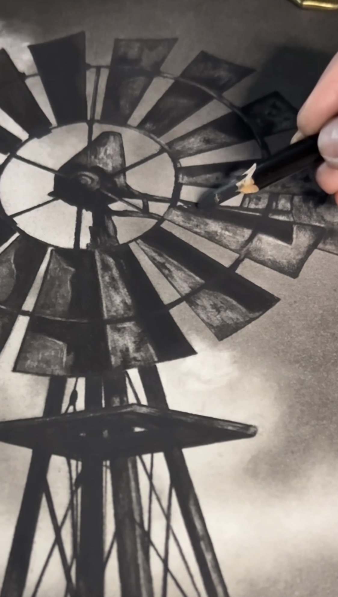 A hand holding a pencil sketches a windmill with a clock face on paper.
