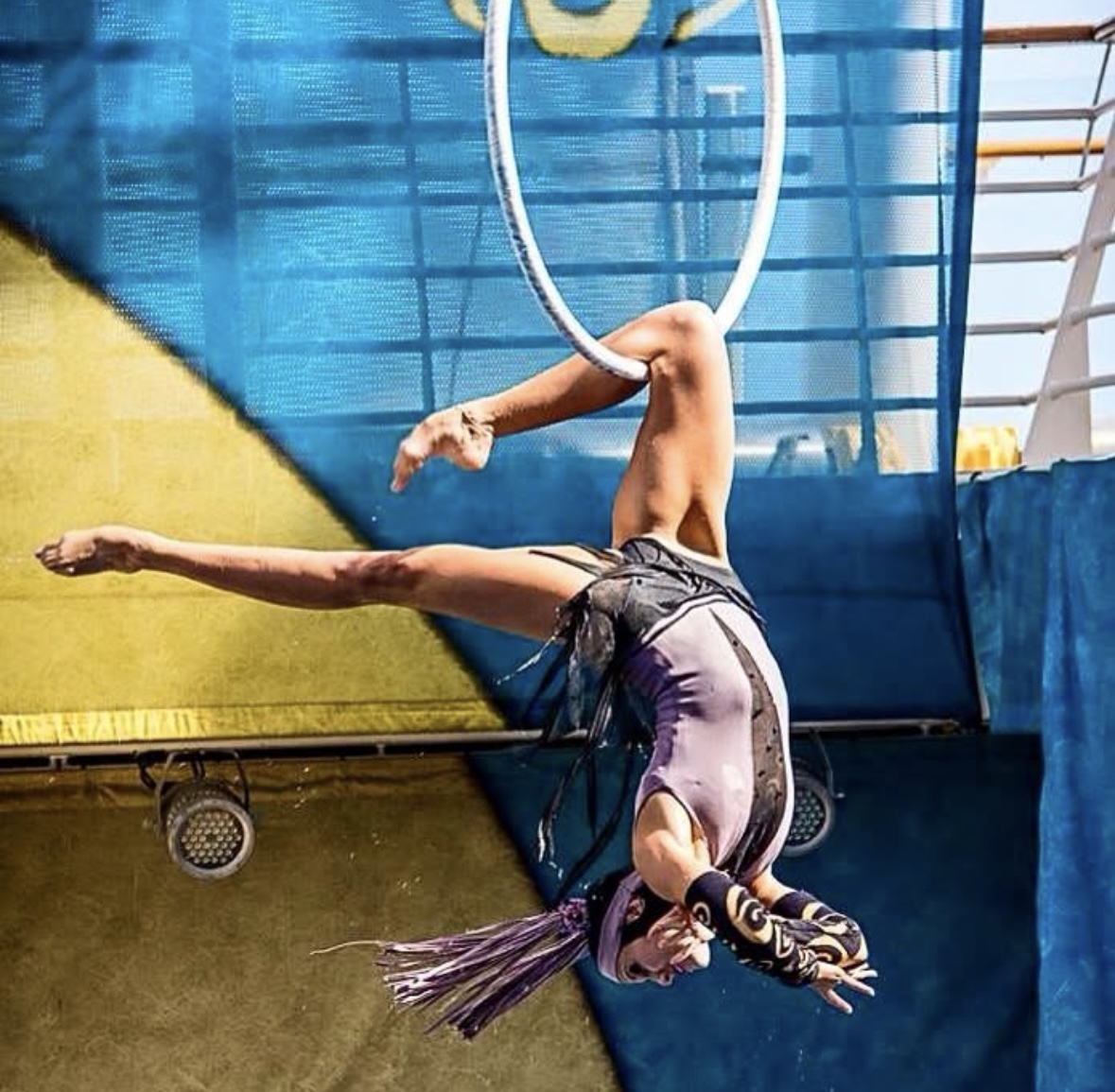 A person performs an acrobatic move hanging upside down from a hoop, with legs extended and arms reaching downward.