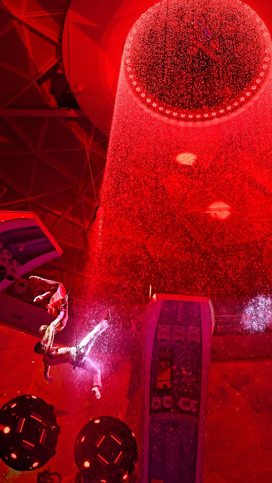 Person in protective gear sprays water in a high-pressure jet inside a red-lit environment.