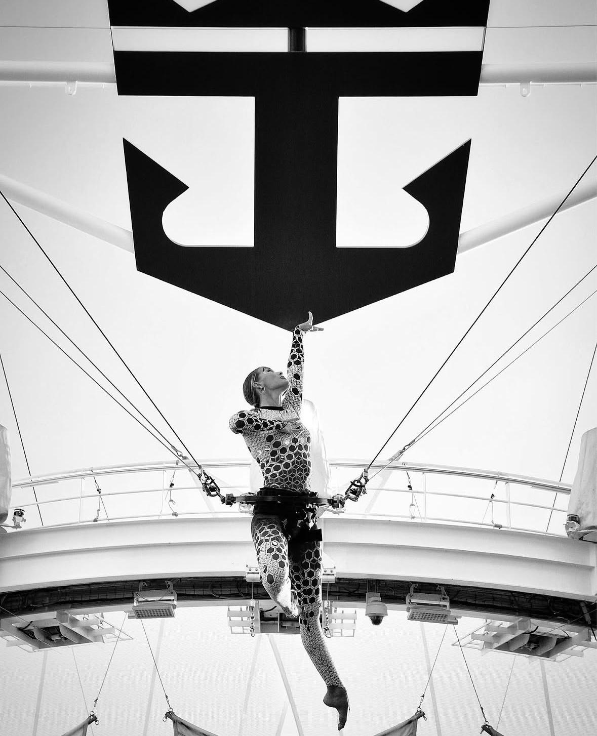 A person in a polka dot outfit hangs from a harness inside a large, modern space with a high ceiling.