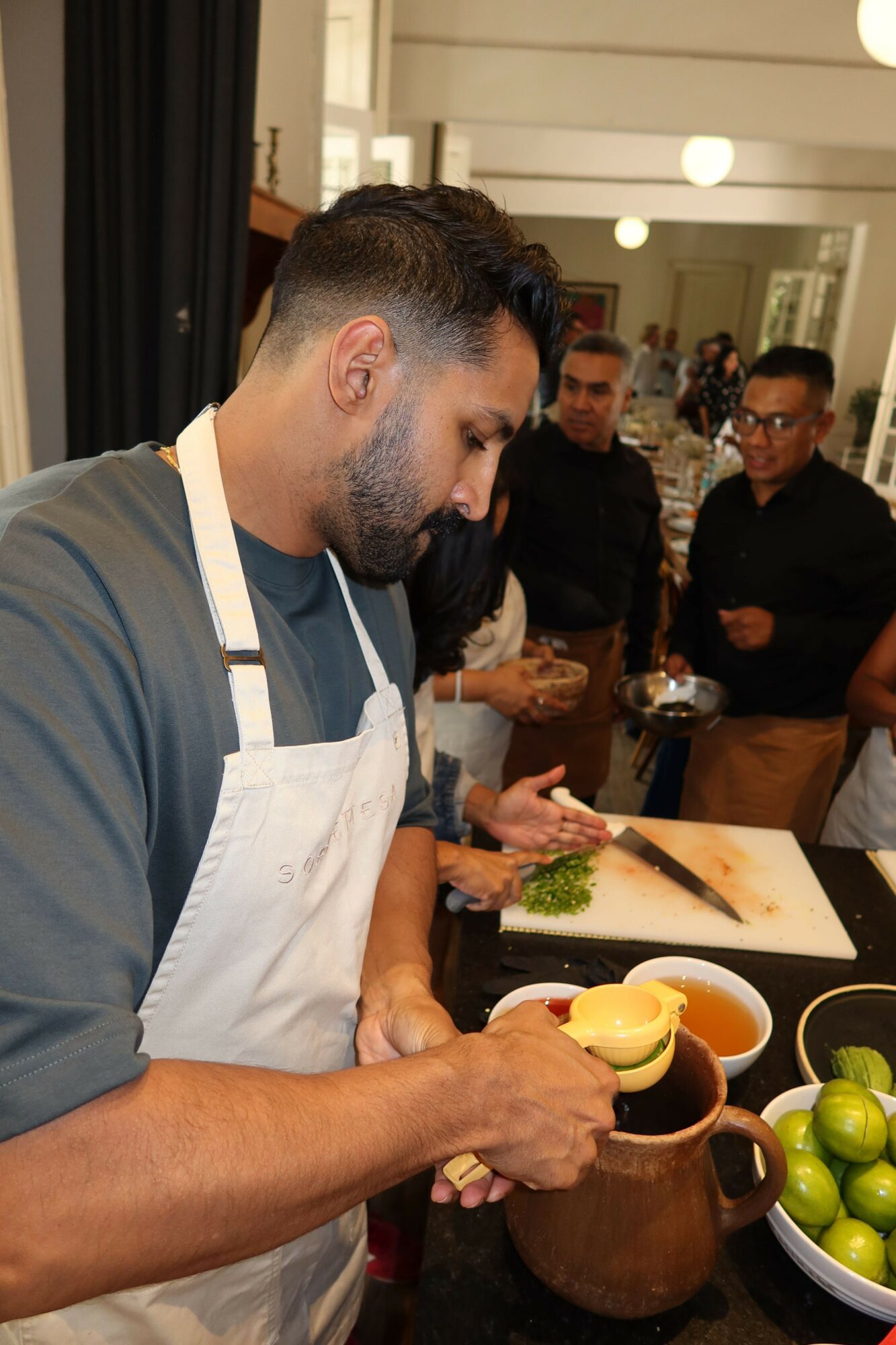 Man with beard and short hair eating at a table with food and drinks, others in background, indoor setting.