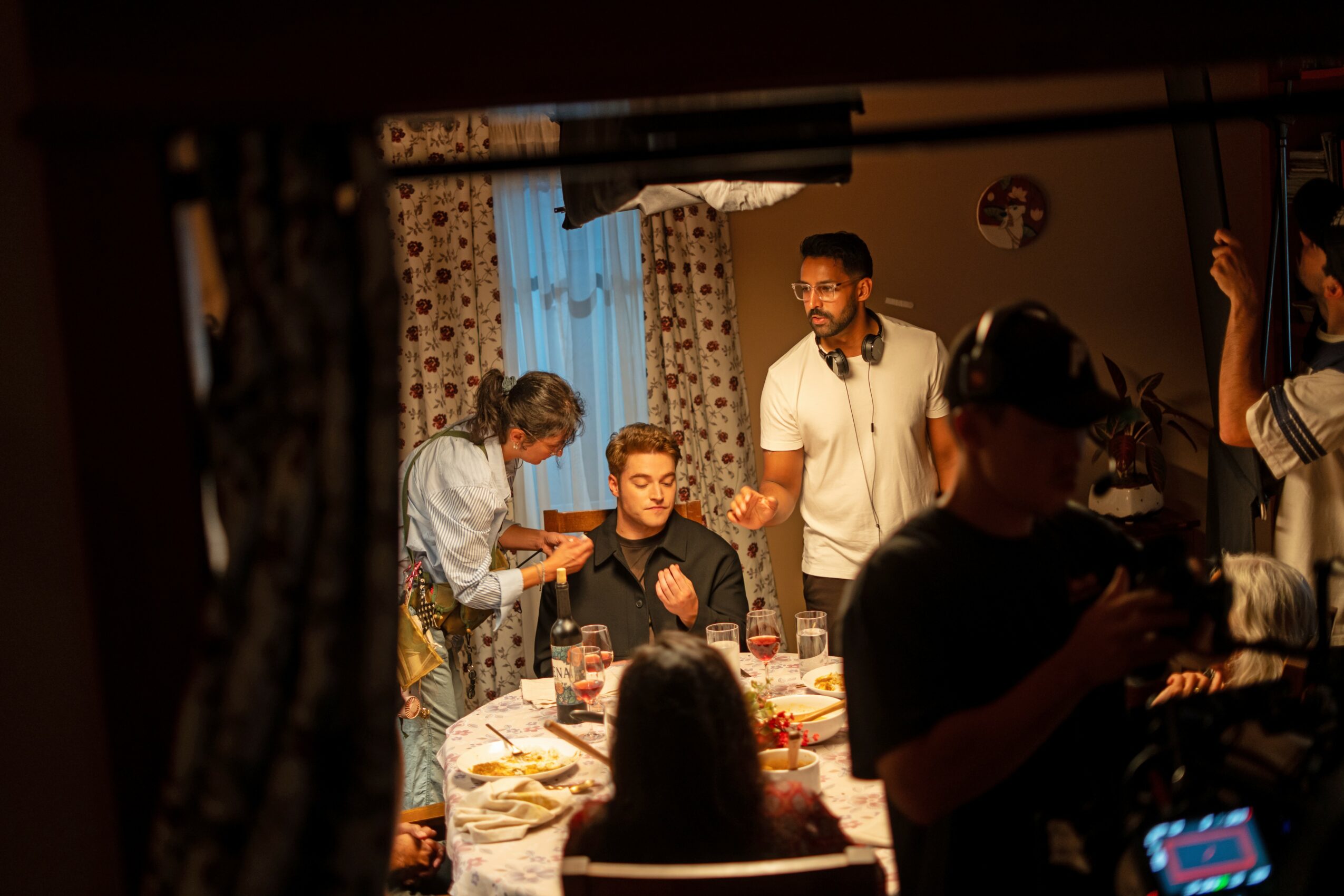 Group of people gathered around a table with food, some standing and some sitting, in a warmly lit room.