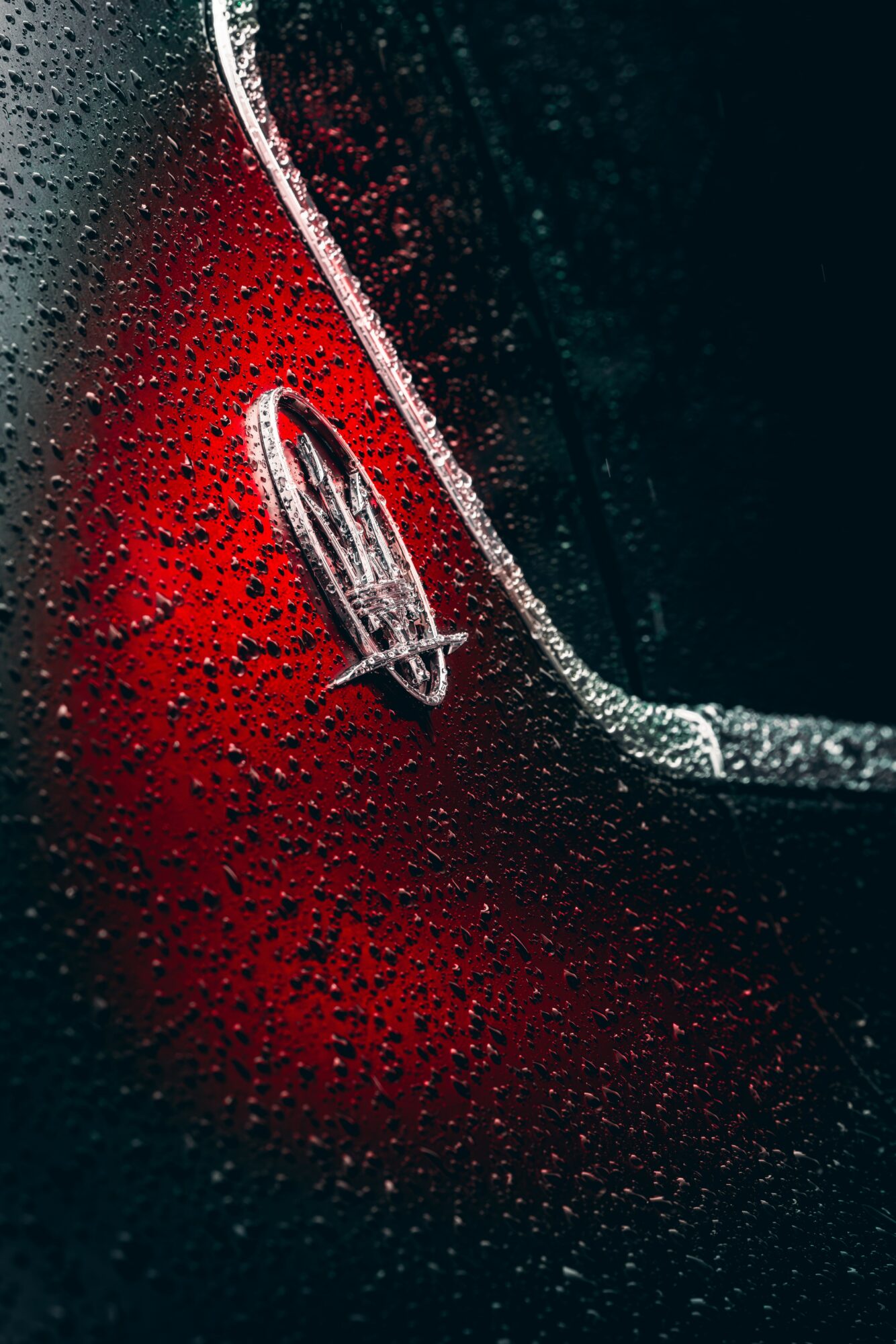Close-up of a car's rear with water droplets, showing a red and black surface and a silver emblem.