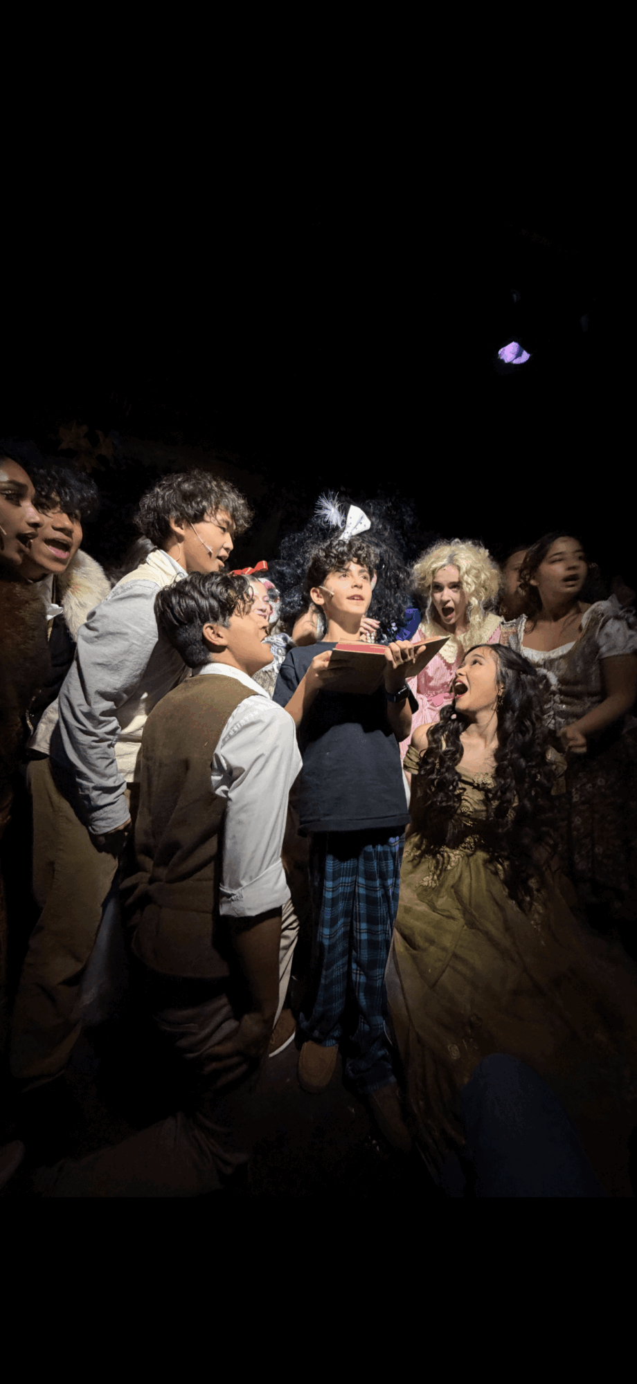 Group of children gathered around a person in a yellow dress, with a dark background and a moon in the sky.