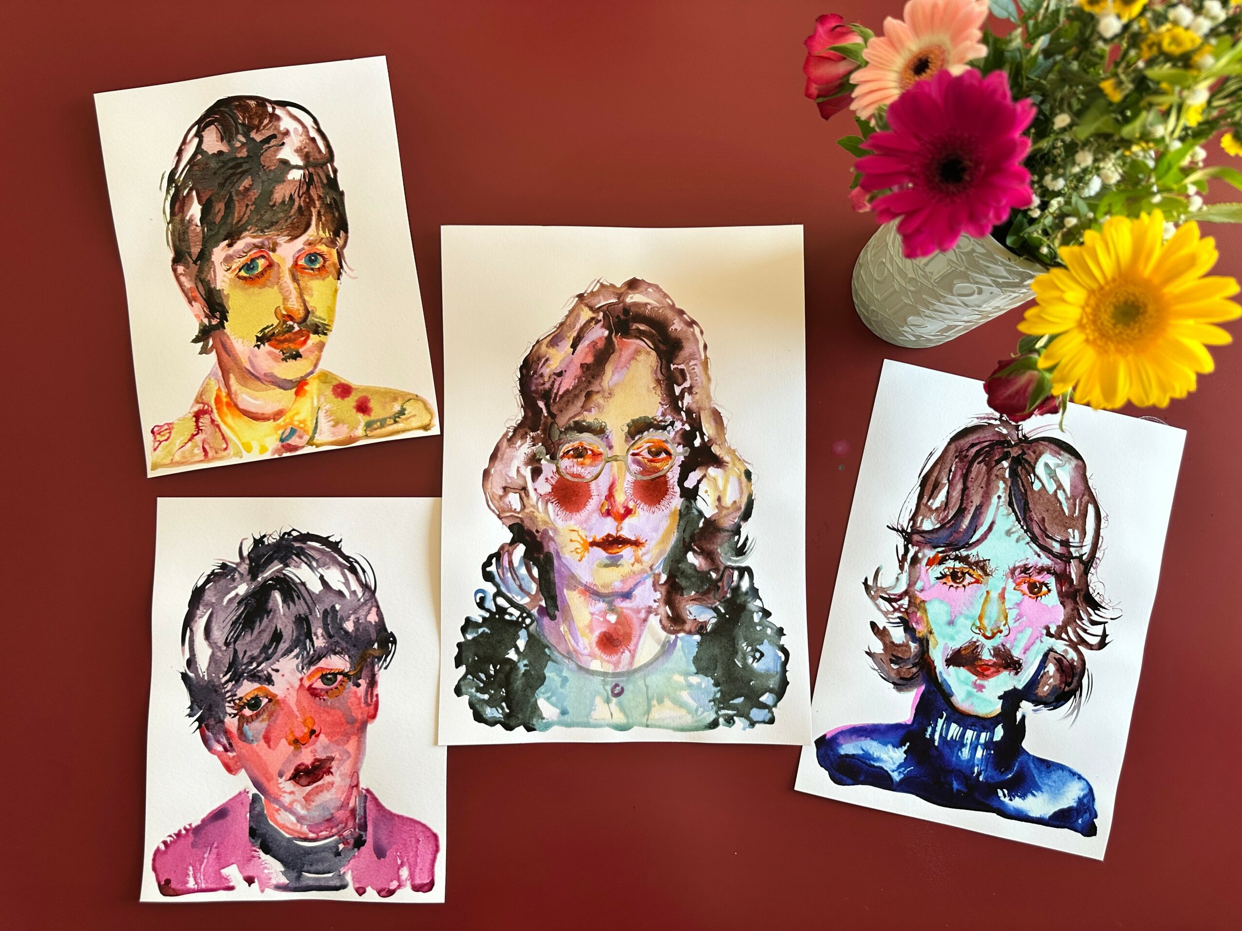 Four colorful portrait illustrations of people arranged on a table with a vase of flowers nearby.