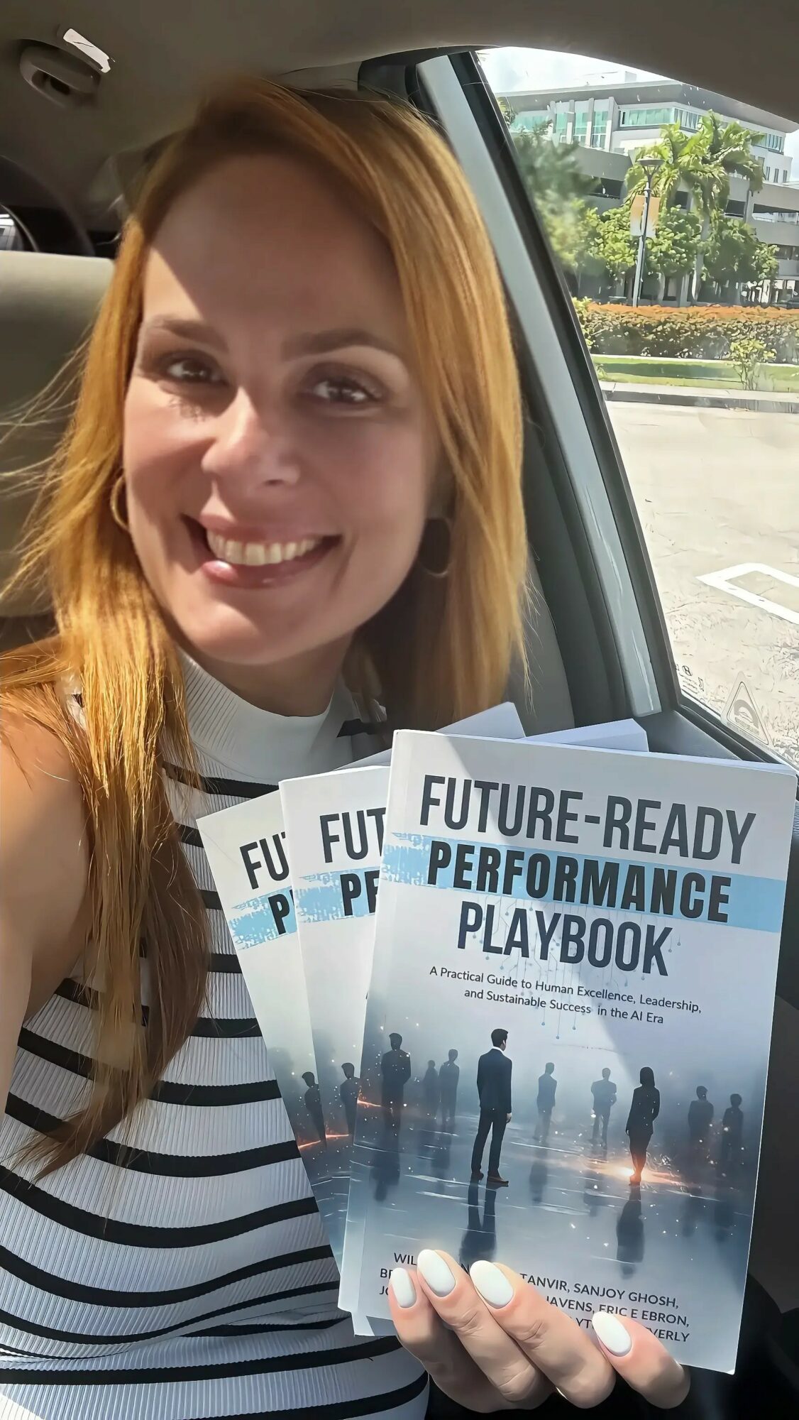 Woman with long red hair smiling inside a car, holding a future-ready performance playbook, with a parking lot outside.