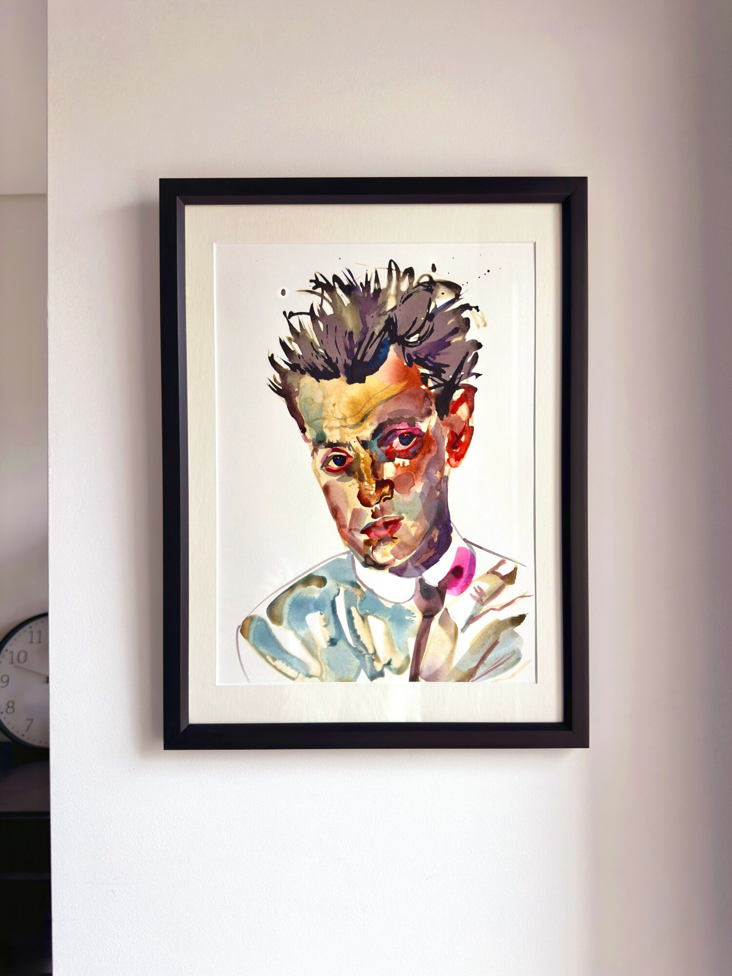 Framed watercolor portrait of a young person with spiky hair, wearing a collared shirt, on a white wall.