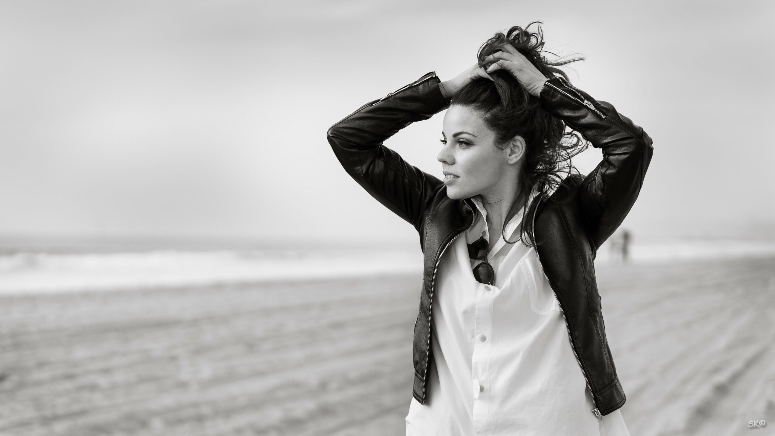 Woman standing on a beach with her hands in her hair, looking to the side, in black and white.