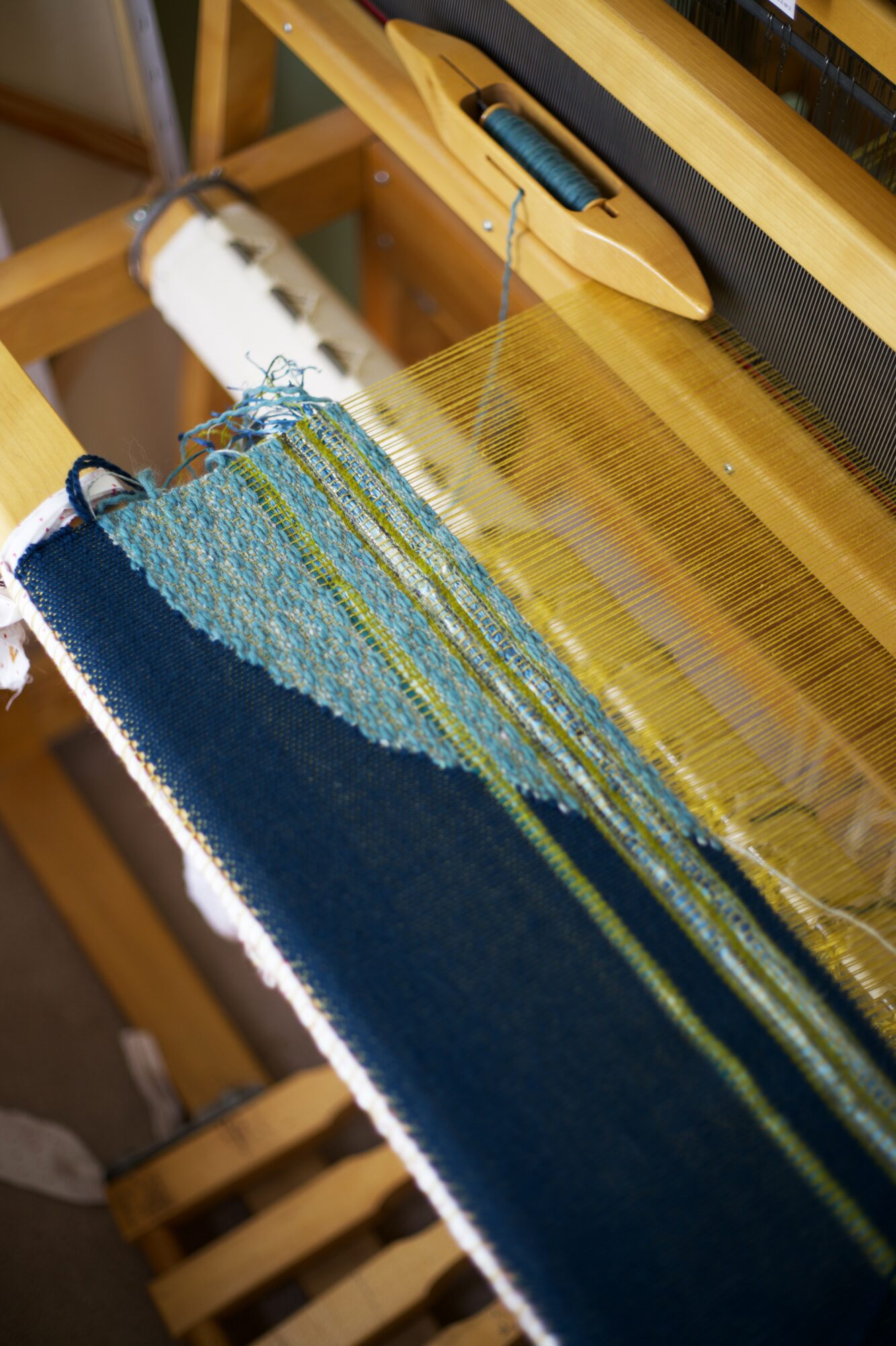 Weaving loom with colorful threads and partially woven fabric, viewed from above.