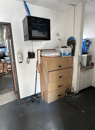 Office corner with a filing cabinet, wall-mounted monitor, and various items on the counter, wall, and floor.