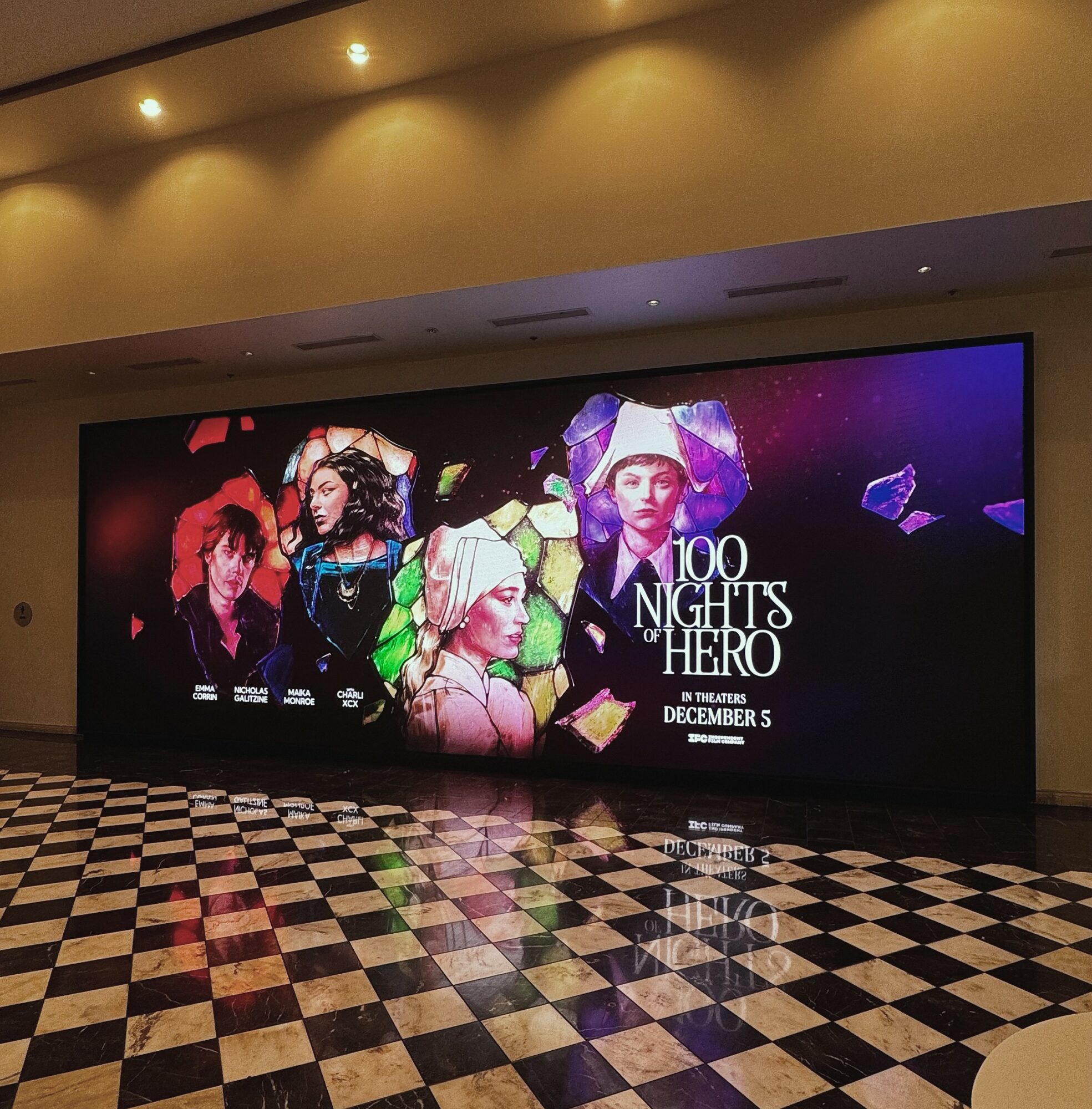 Large digital poster displays four women with colorful backgrounds, advertising '100 Nights Hero' event on December 5.