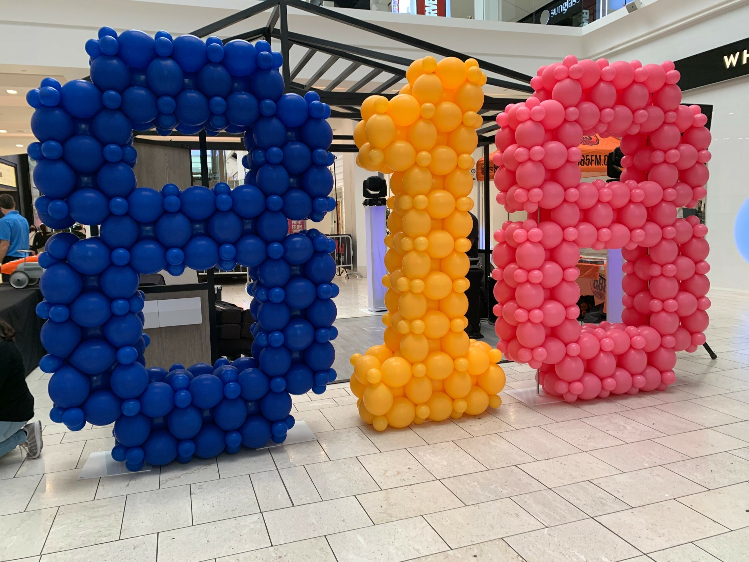 Decorative balloon letters spelling 'A', 'I', and 'O' in blue, yellow, and pink, displayed outdoors on a tiled surface.