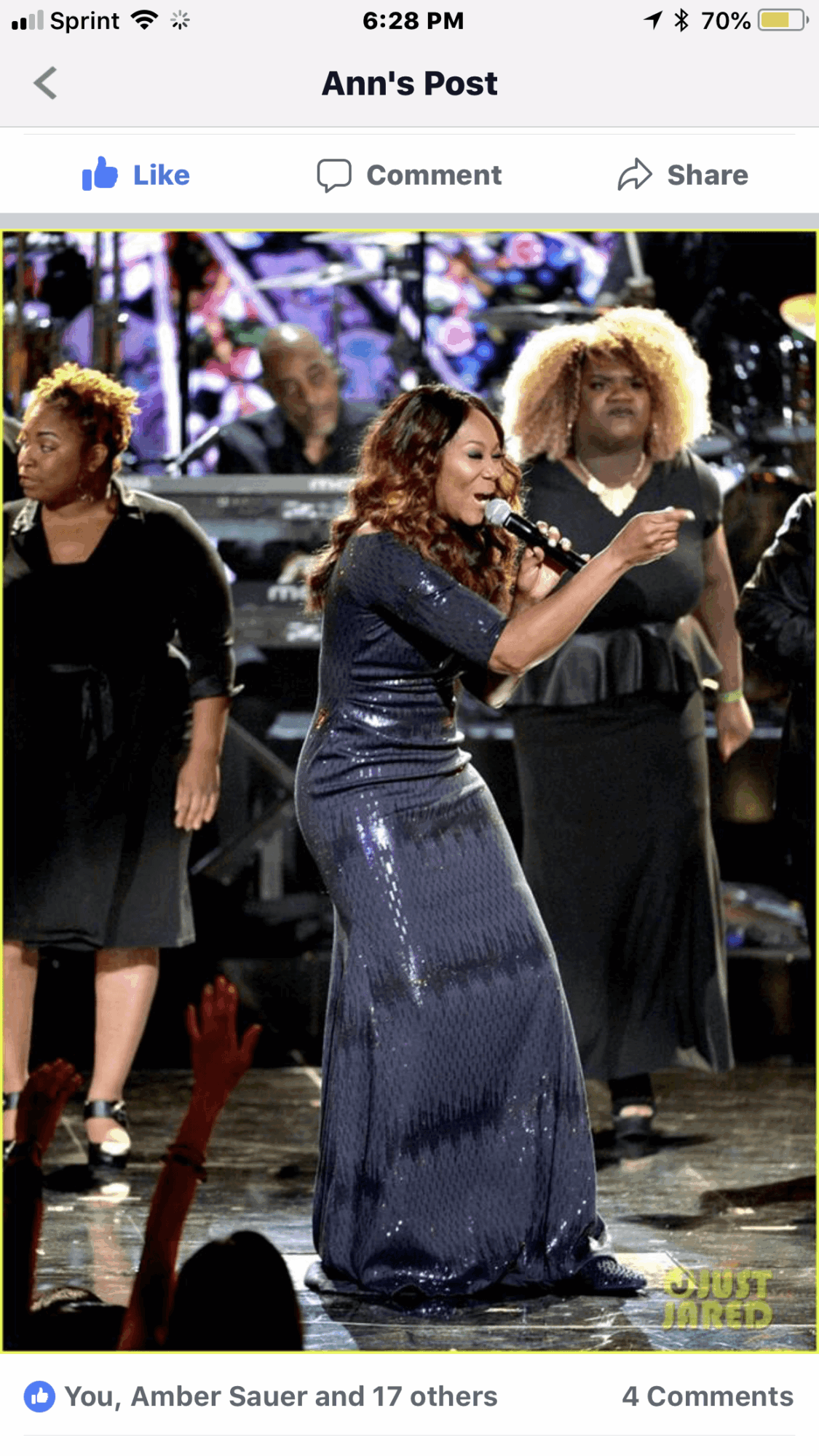 Woman in a long, shiny blue dress dancing on stage with three women in black dresses behind her.