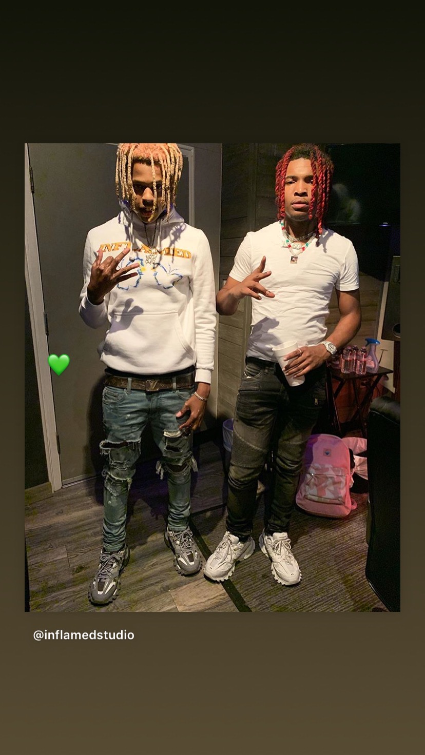 Two young men with dreadlocks pose indoors, one in a white hoodie and jeans, the other in a white t-shirt and black pants.