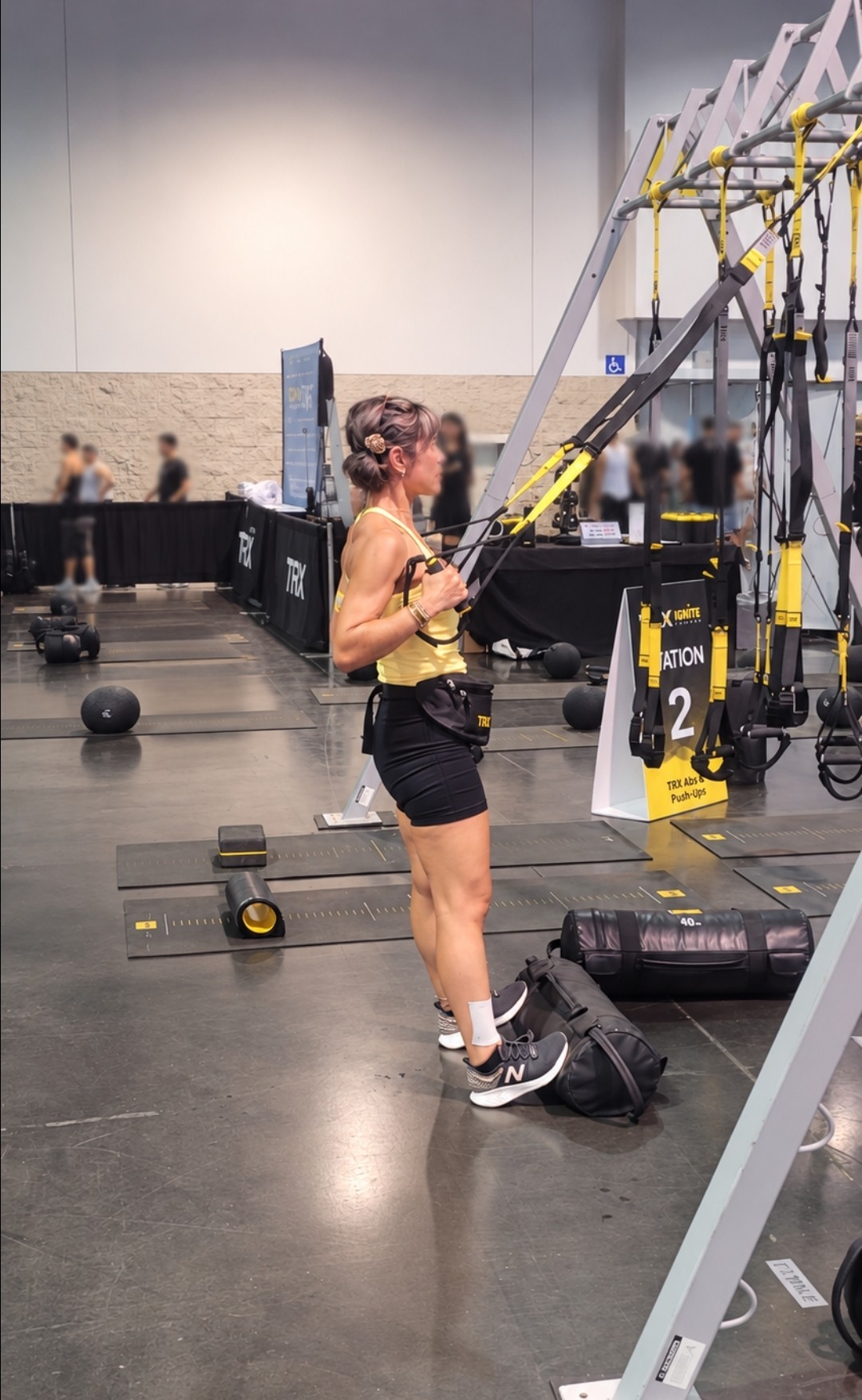 Woman using suspension training equipment in gym, with other workout stations in background.