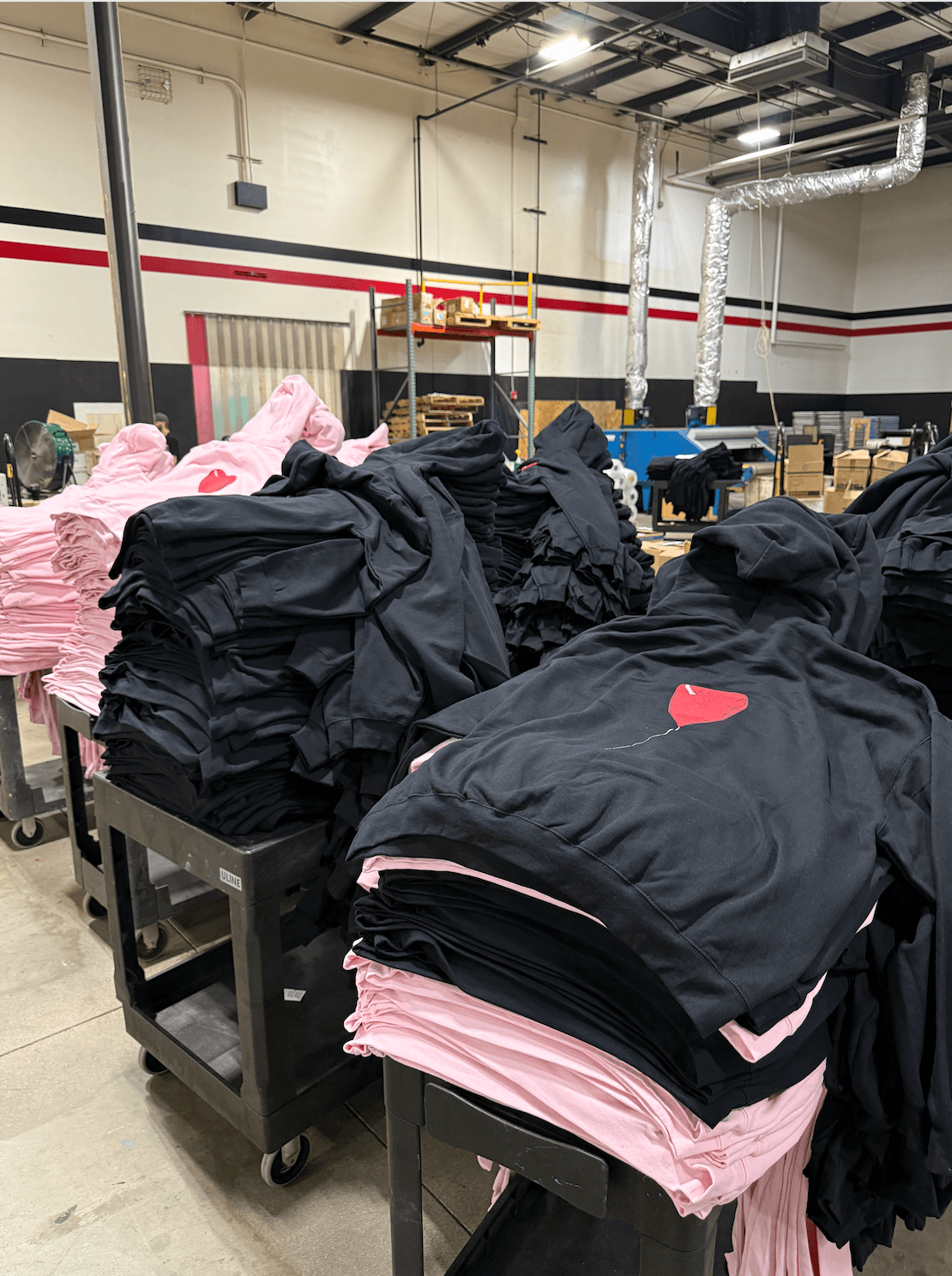 Stacks of black hoodies with red Nike logos and pink clothing on black carts in a warehouse setting.
