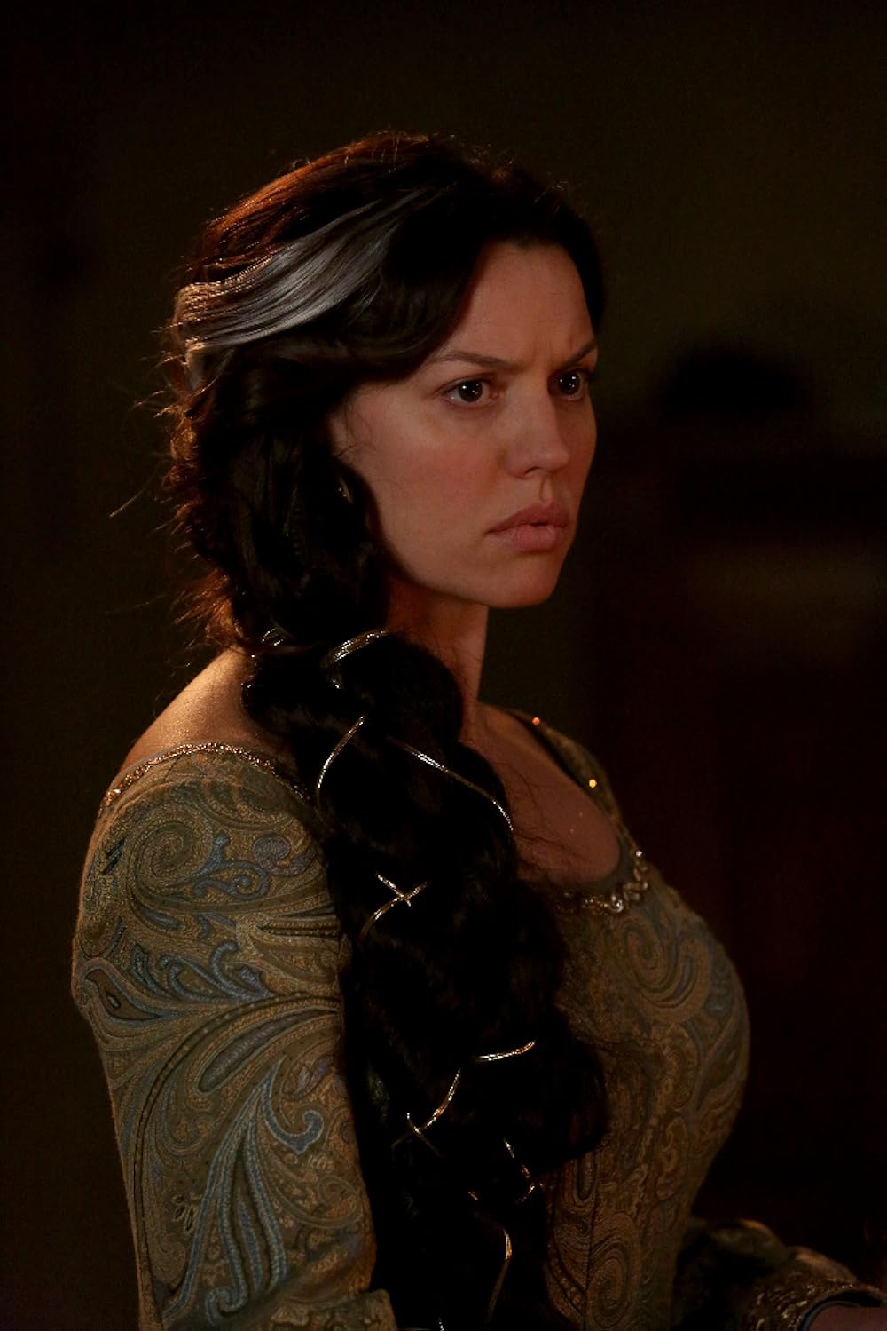 Woman with long dark hair and a serious expression, wearing a patterned top, facing slightly to the right.