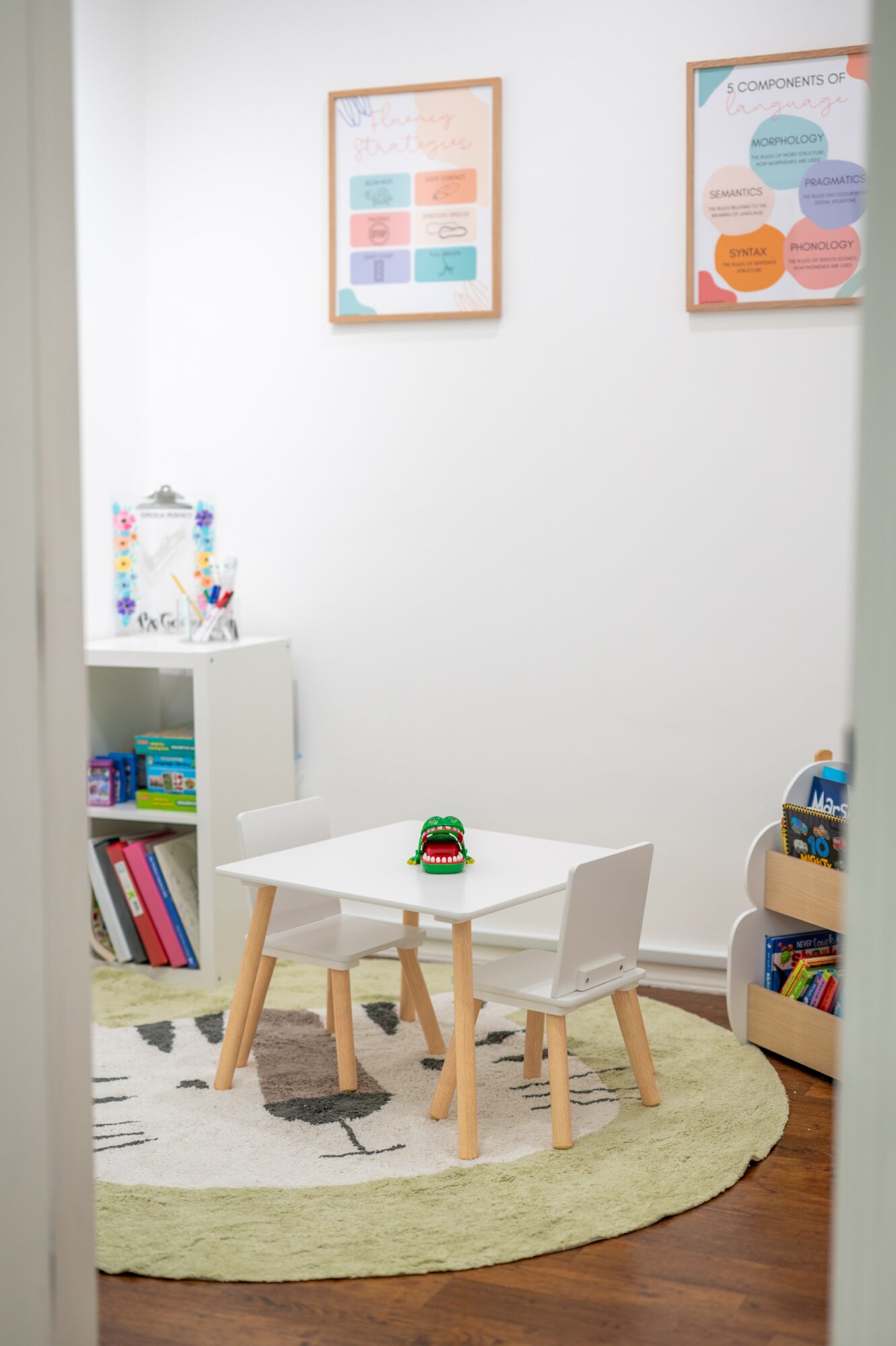 Children's play area with a white table, two chairs, a round rug, and wall posters in a room.