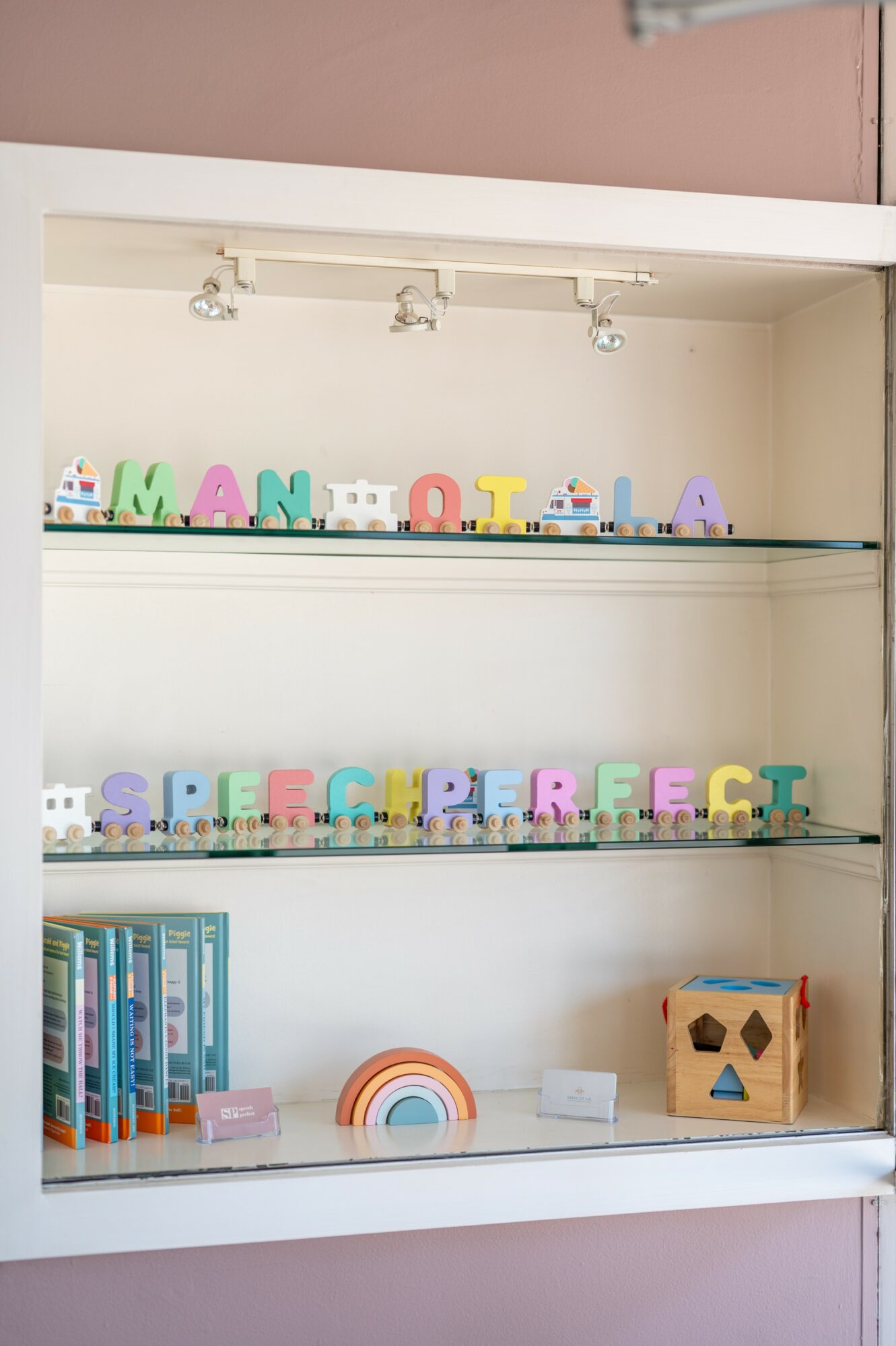 Shelves with colorful alphabet blocks, books, and a rainbow decoration, against a pink wall background.