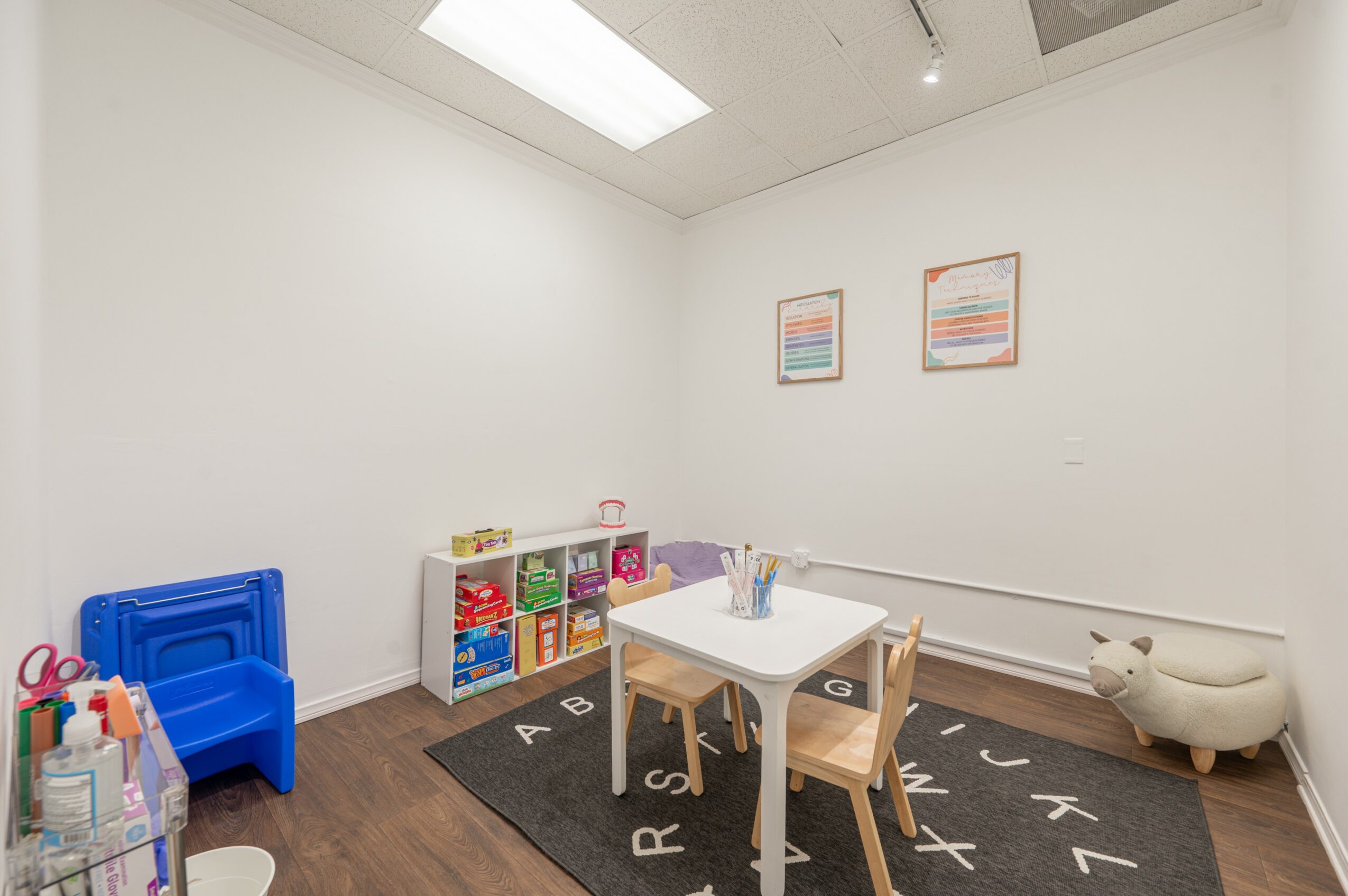 Children's playroom with a white table, chairs, colorful toys, and wall art, on a black rug with letters.