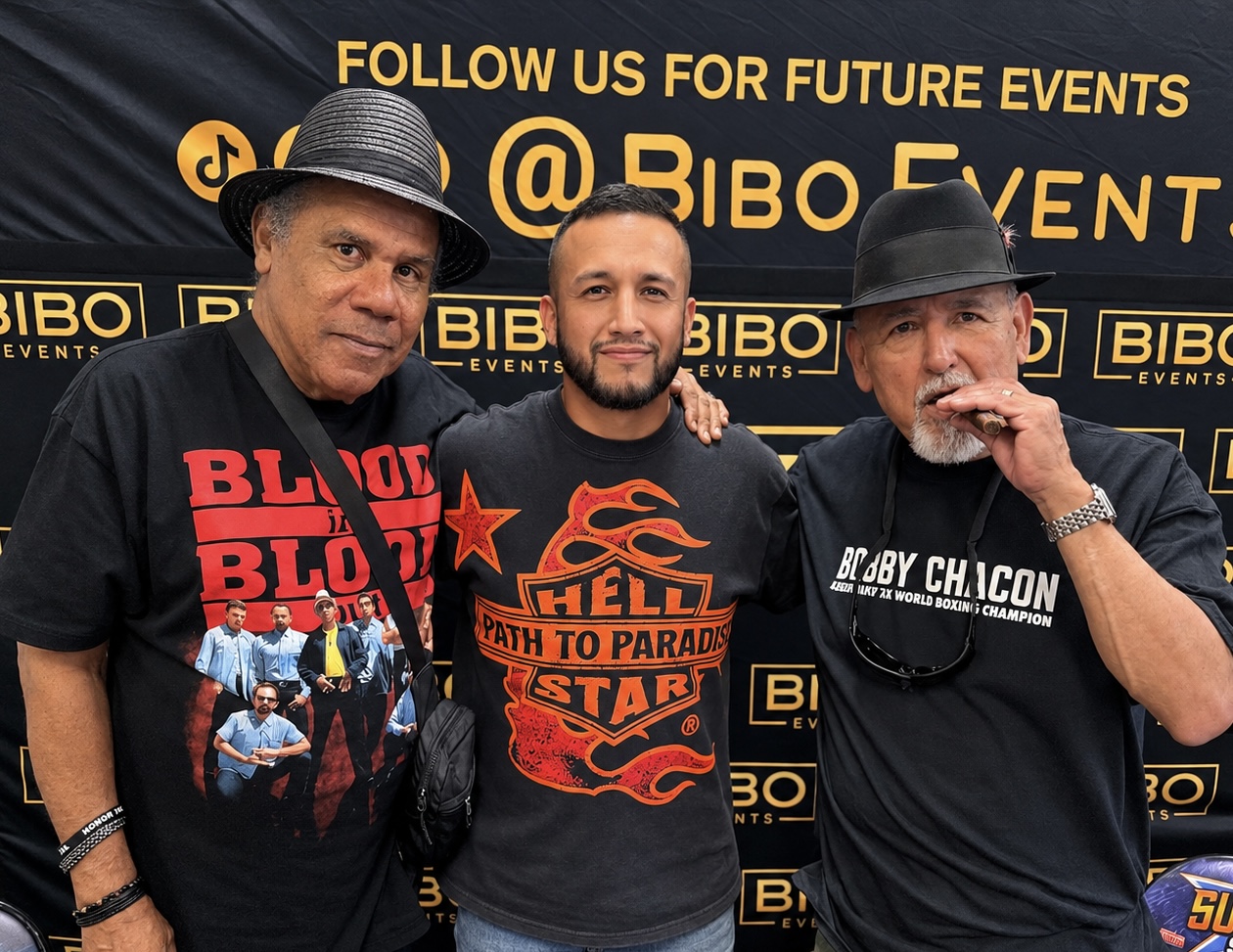 Three men standing in front of a black backdrop with yellow text and logos, smiling and posing for the photo.