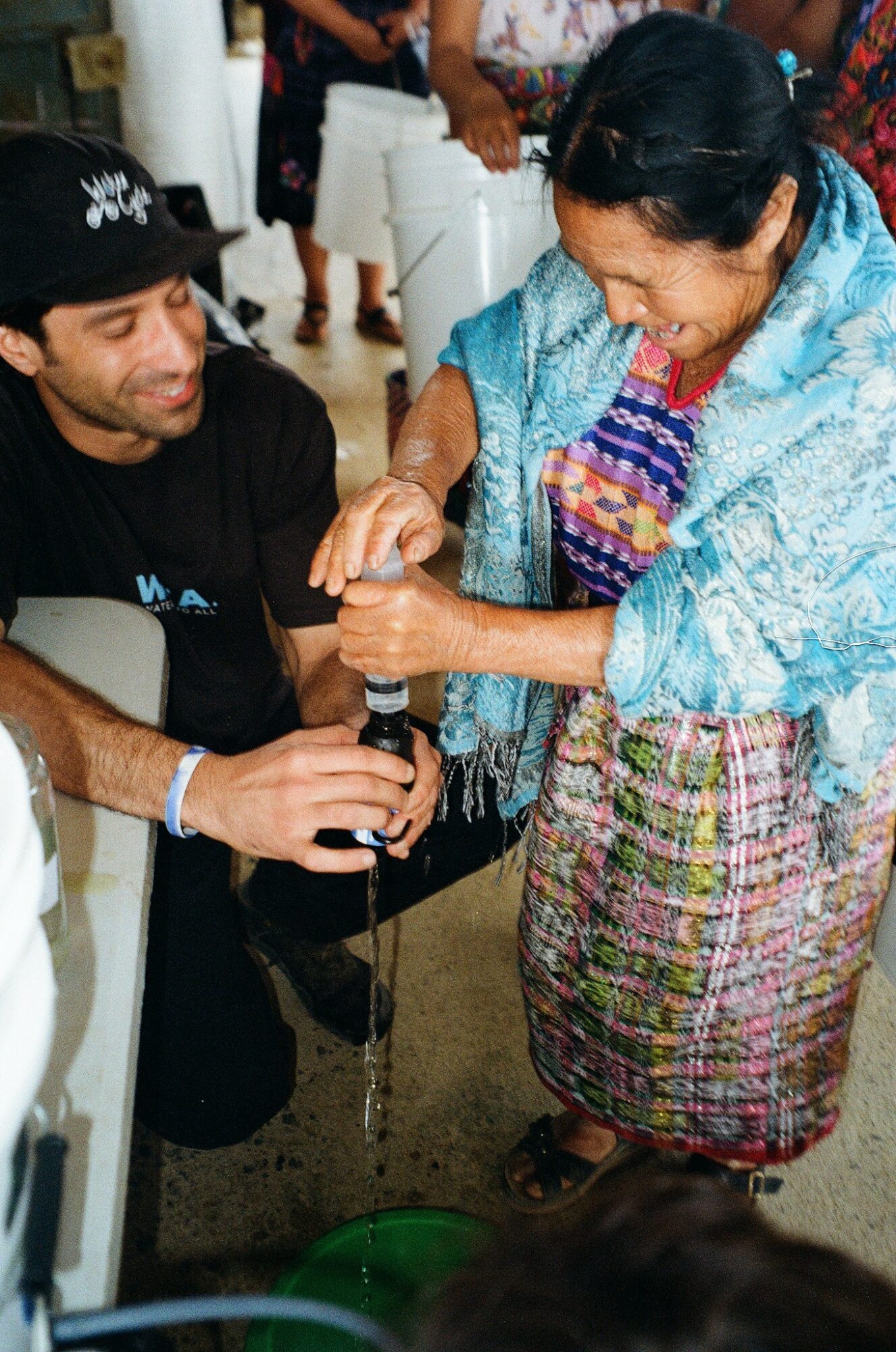 A woman and a man are pouring water together into a container, smiling and engaging in a shared activity.
