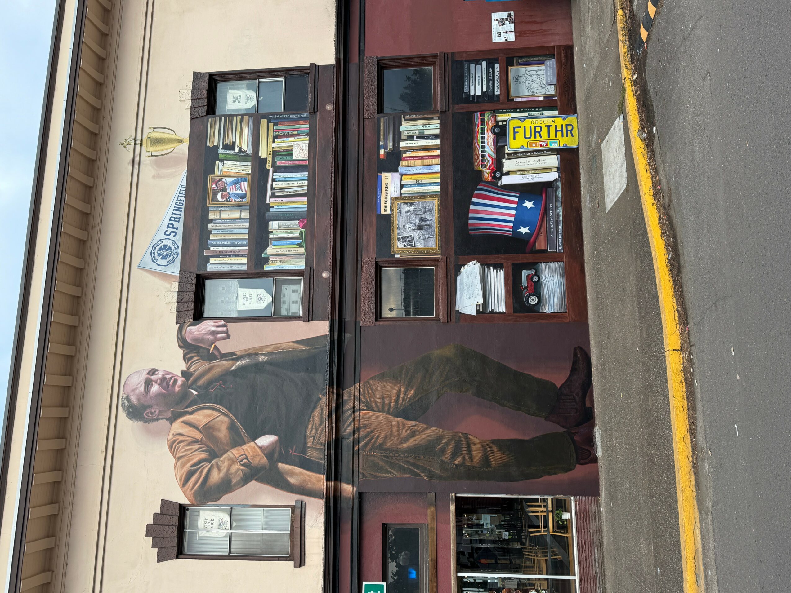 Person standing outside a bookstore with glass display windows filled with books, on a sidewalk with a yellow line.
