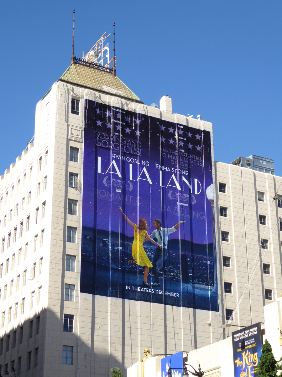 Large vertical poster on building shows two dancers, one in yellow and one in blue, dancing against a starry night sky background.