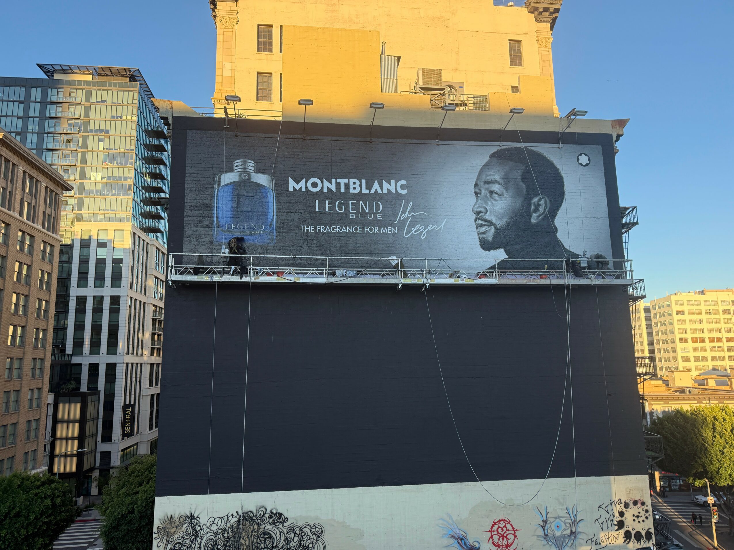 Billboard on building features a man with a beard and a logo, with city buildings in the background.