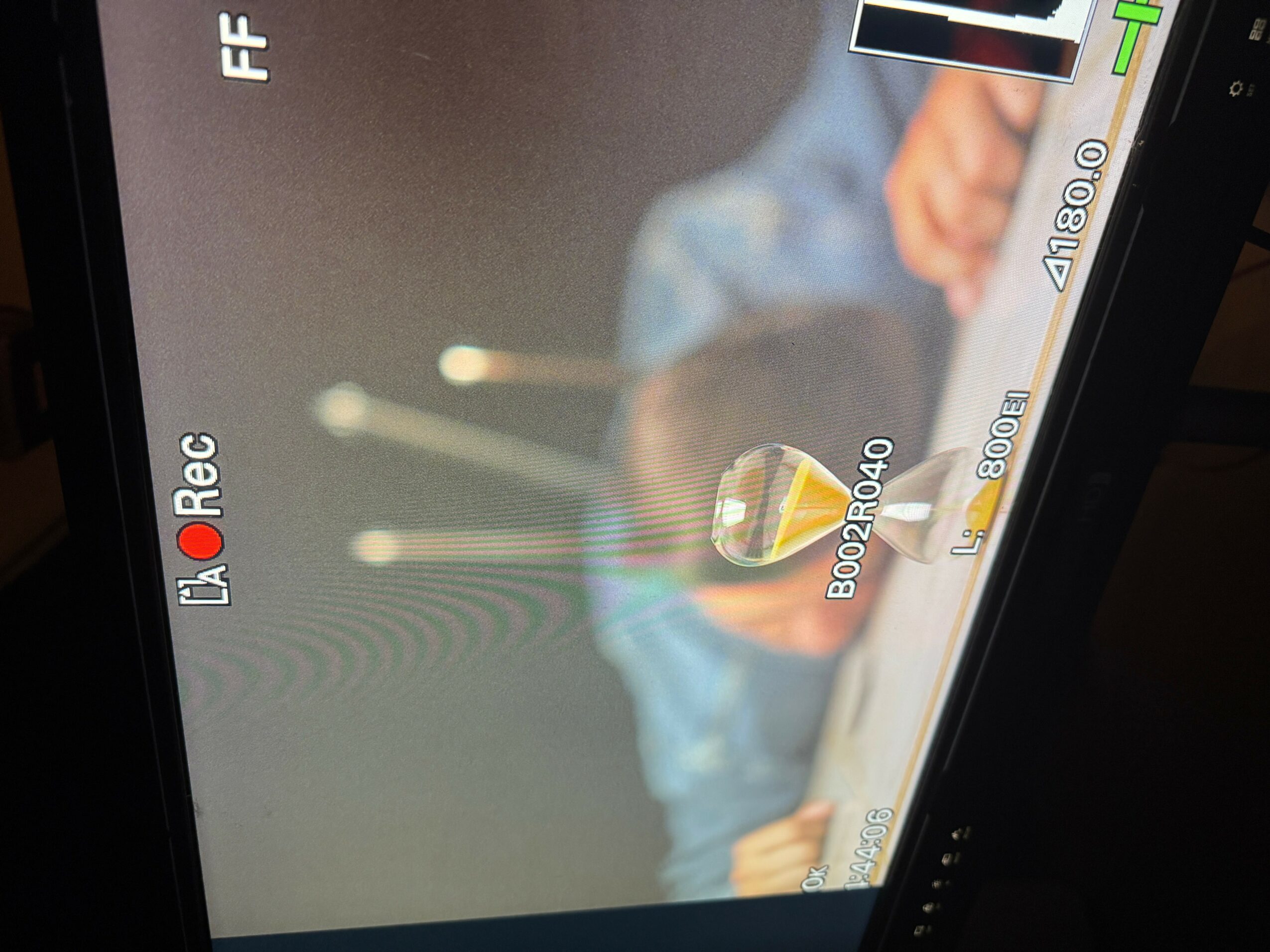 Person holding a glass with a drink, blurred background, camera viewfinder overlay, recording indicator, and settings icons.