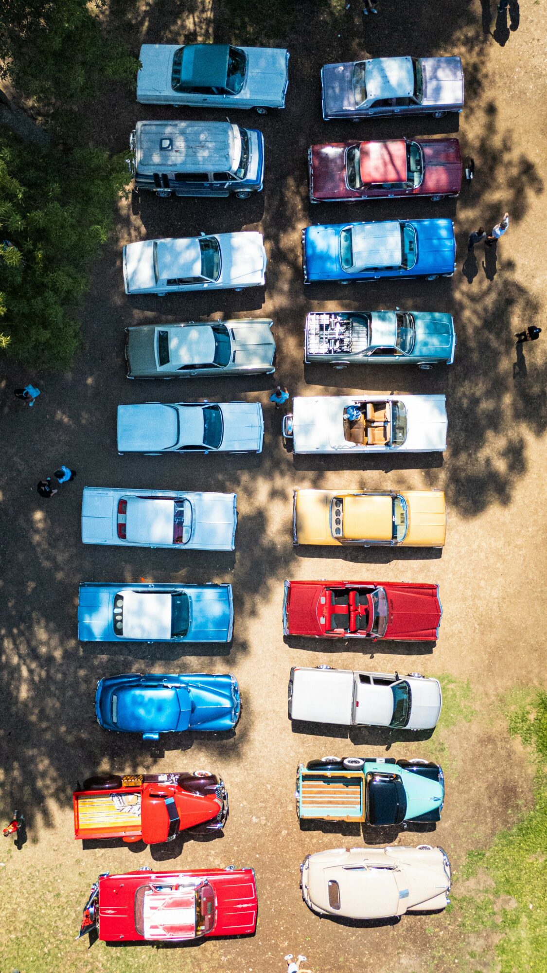 Multiple parked cars in a lot, viewed from above, with trees and dirt areas nearby.