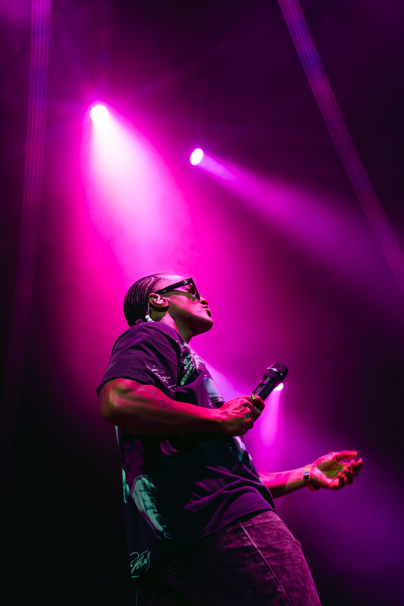 Performer holding a microphone on stage with purple lighting overhead.