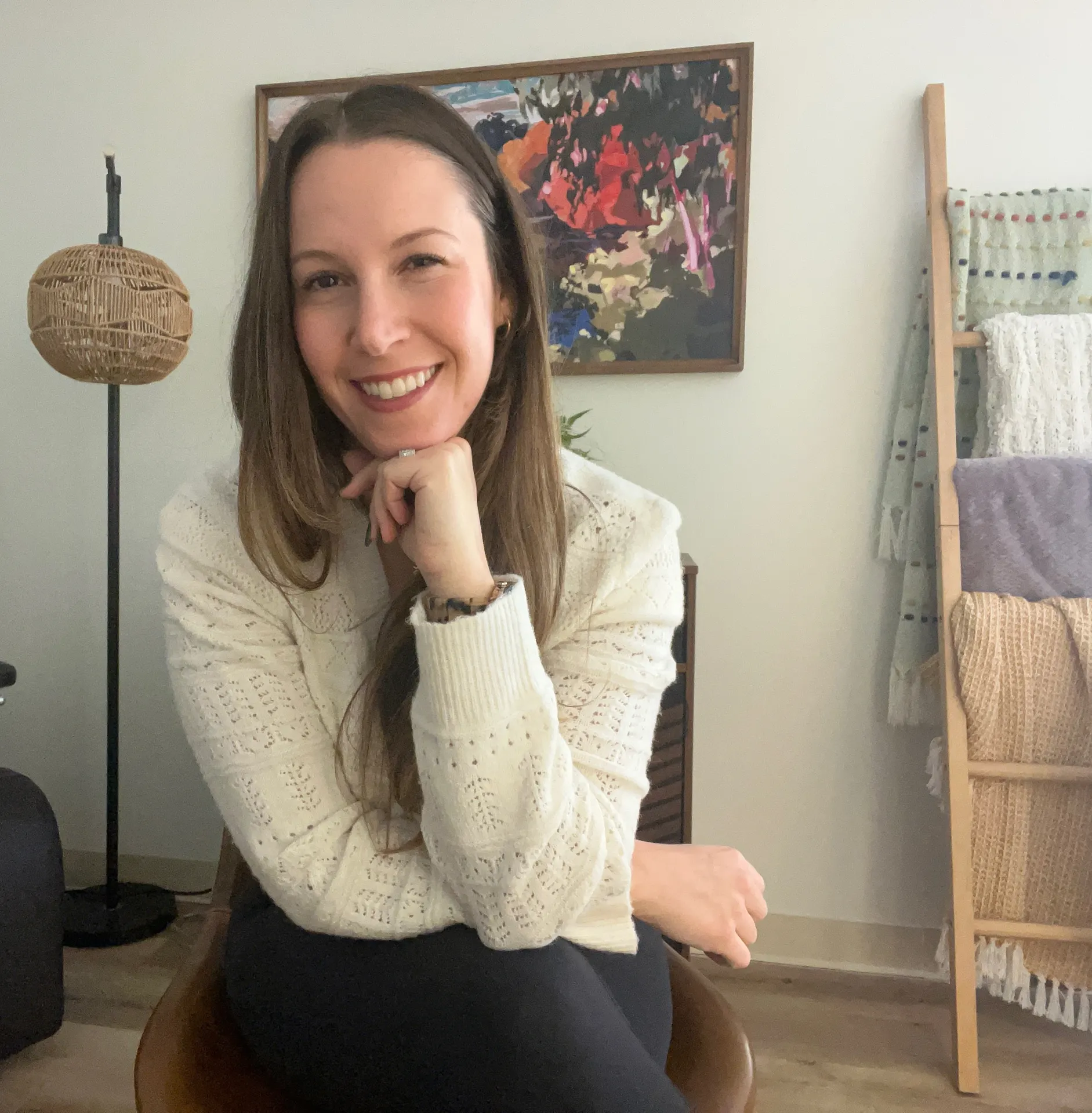 Woman smiling, sitting on a chair, in a room with artwork and a wooden ladder with textiles.