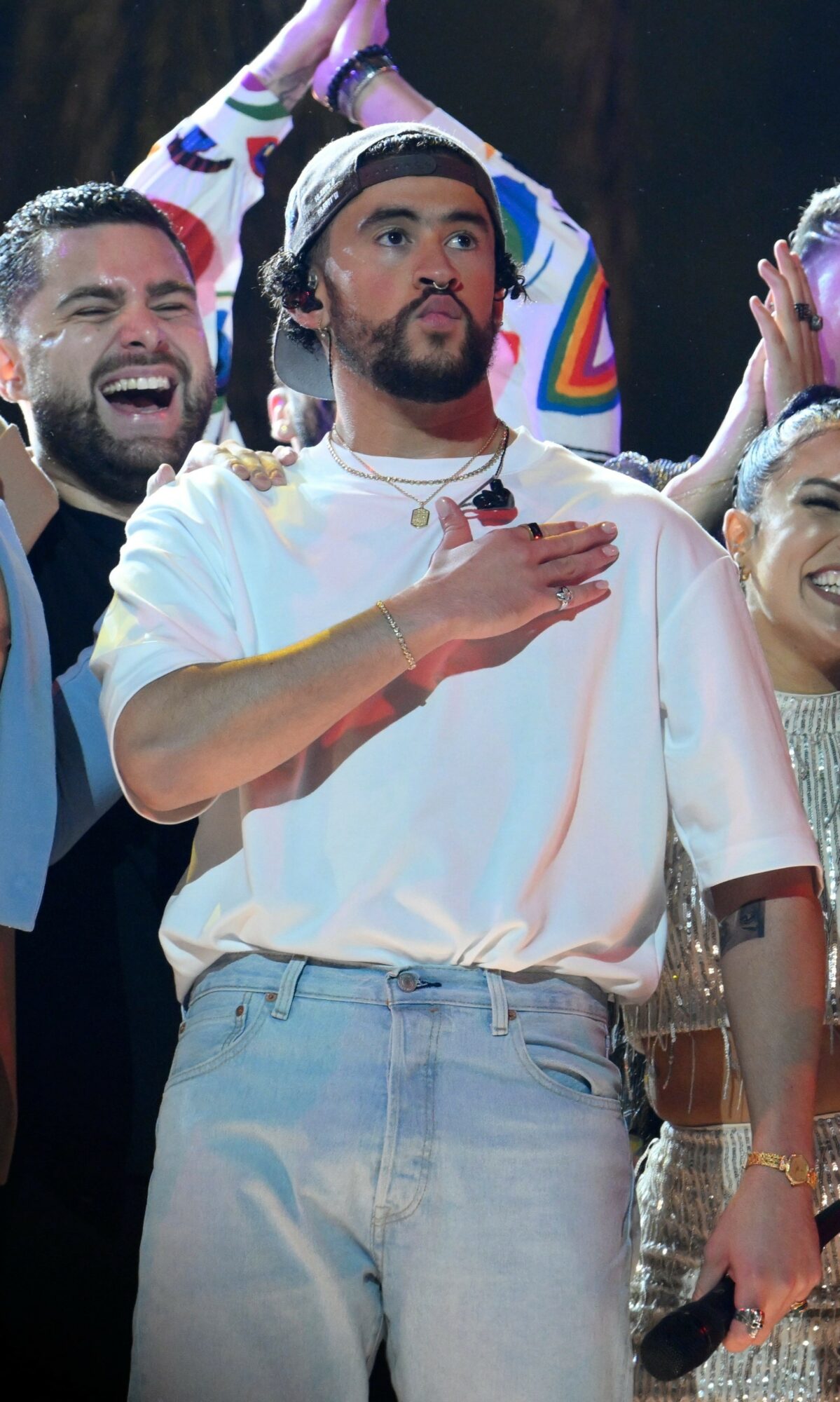 Group of people celebrating, one person with hand over heart, smiling, wearing casual clothes, in a festive setting.