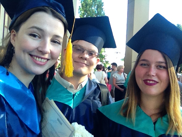 Three graduates in caps and gowns smiling at the camera outdoors.