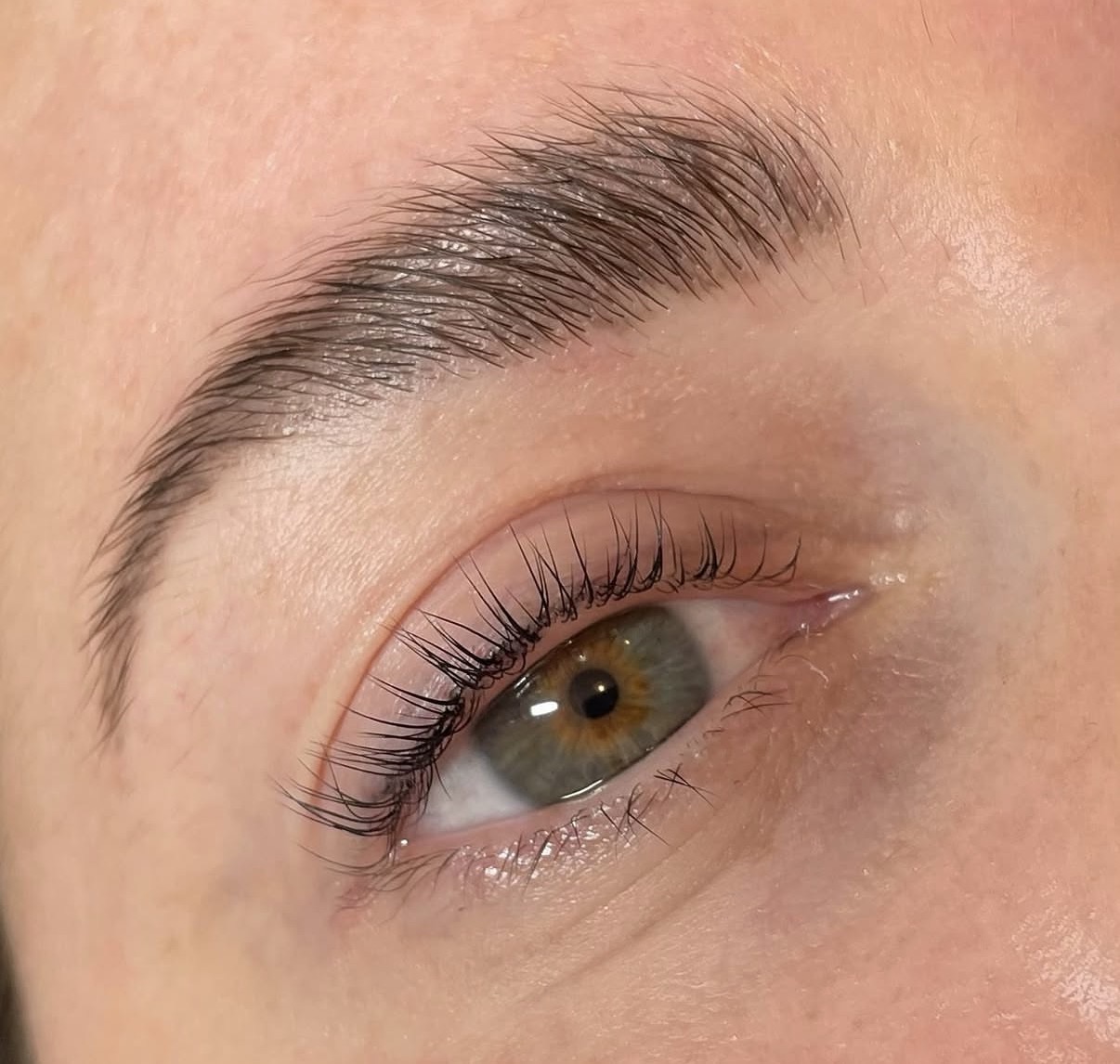 Close-up of a person's eye with a well-groomed eyebrow and long eyelashes, light skin, and greenish eye color.