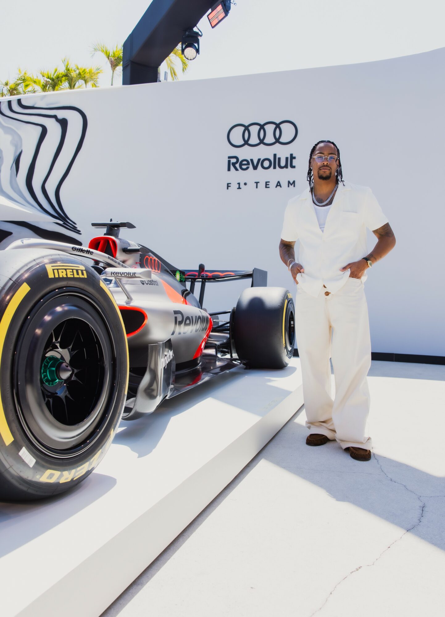 Person standing next to a race car on display at an event, with a white wall and logo in the background.