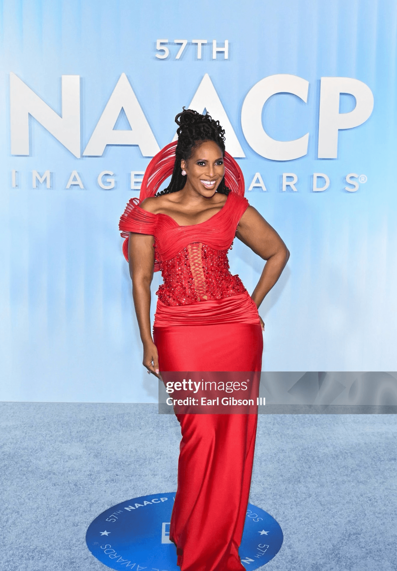 Woman in red gown standing on stage at NAACP Image Awards, smiling, with blue backdrop and event logo.