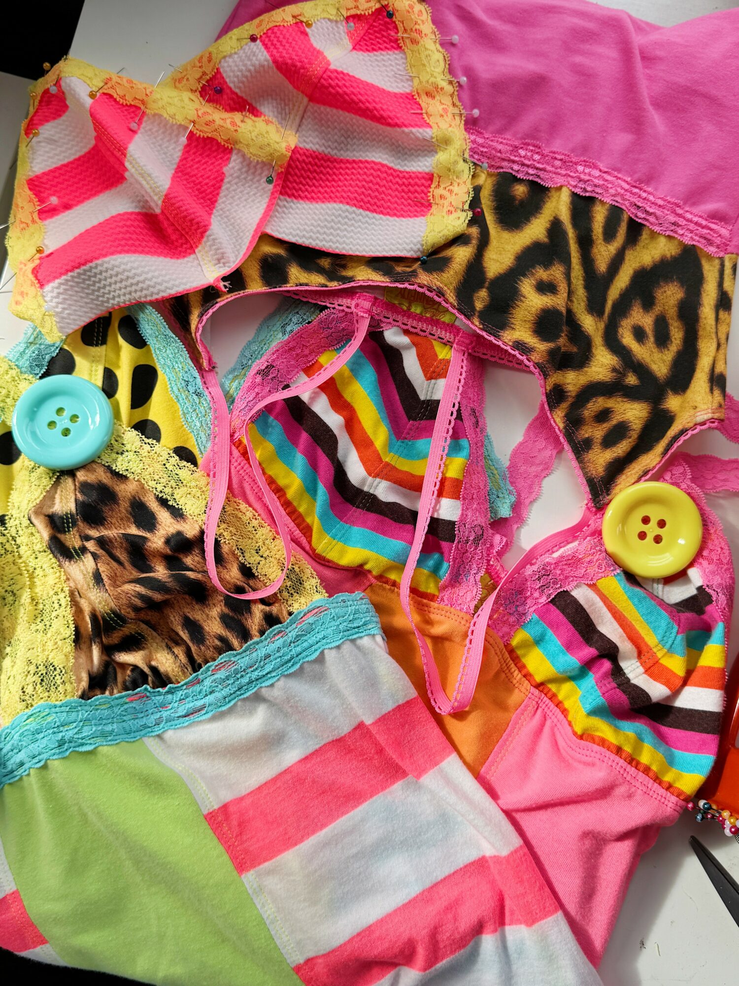 Colorful children's clothing with stripes, animal prints, buttons, and lace details, arranged in a pile.