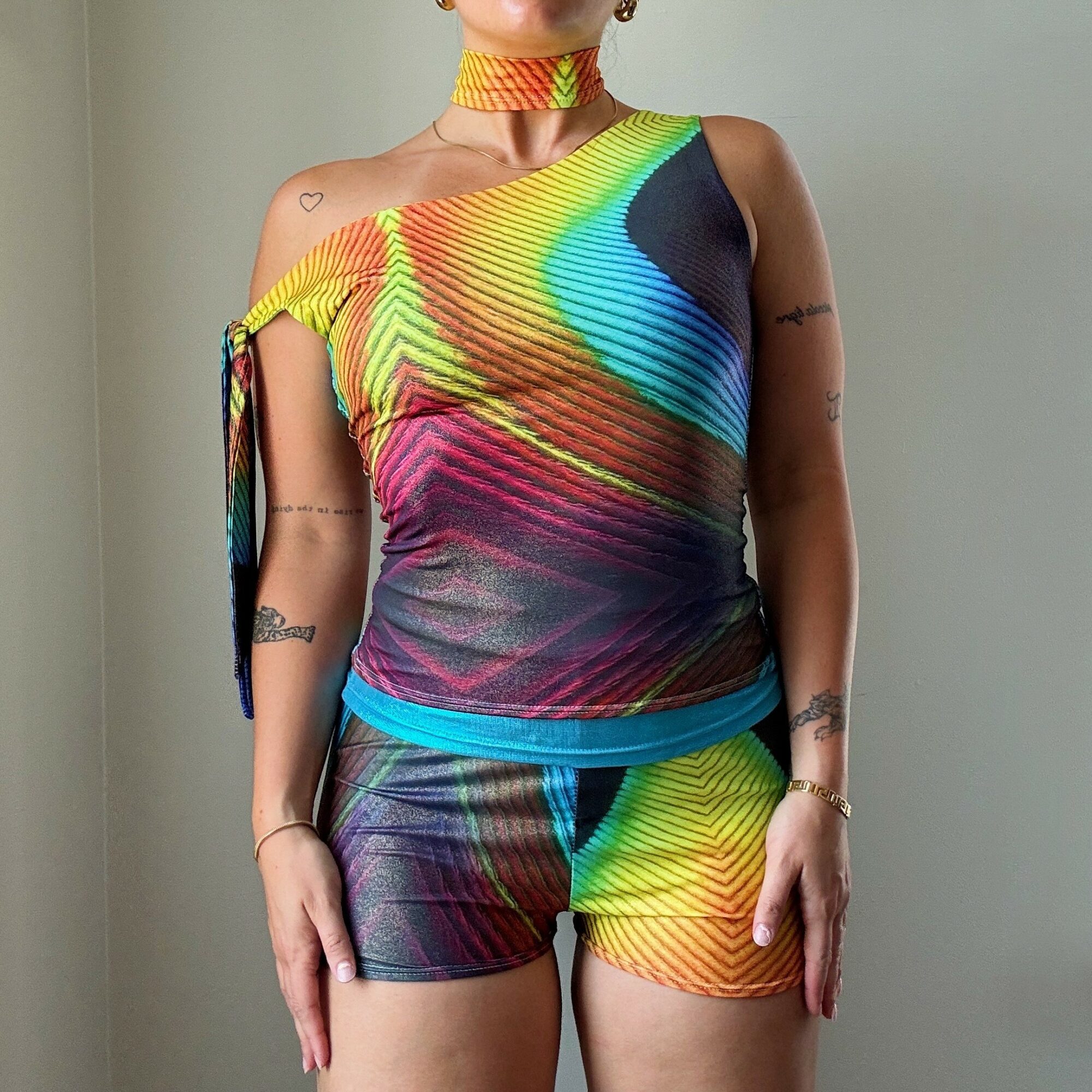 Person wearing a colorful, rainbow-patterned sleeveless top and matching shorts, standing against a plain background.