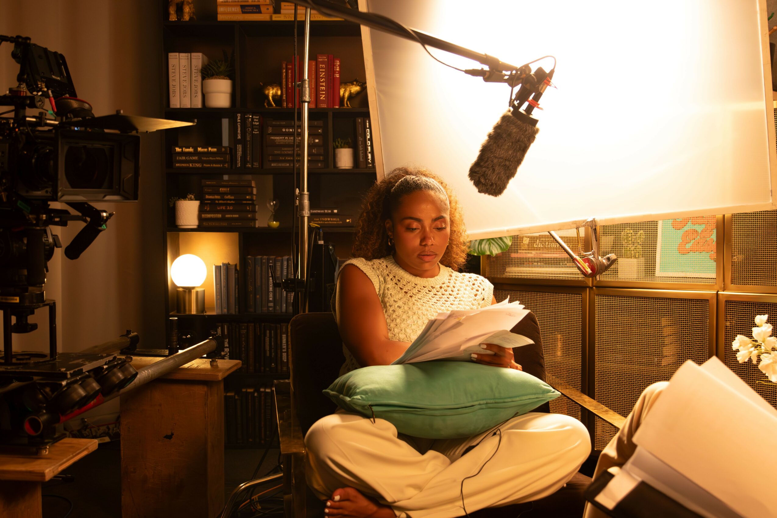Woman sitting on a cushion reading a script in a recording studio with a boom microphone overhead.