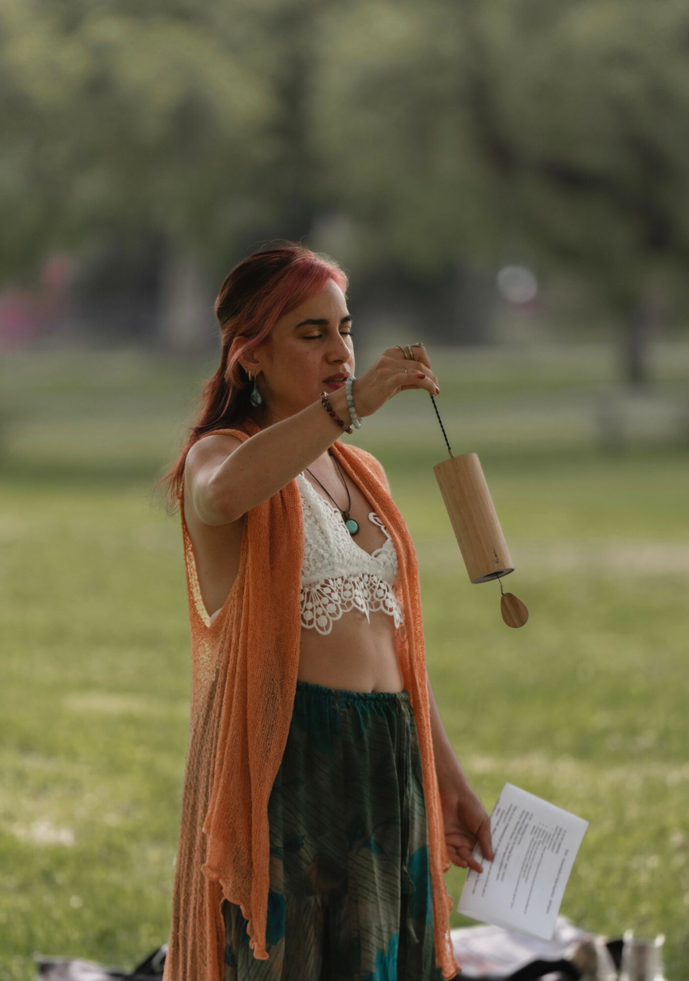 Woman with pink hair holding a wind chime outdoors, holding a paper in her other hand.