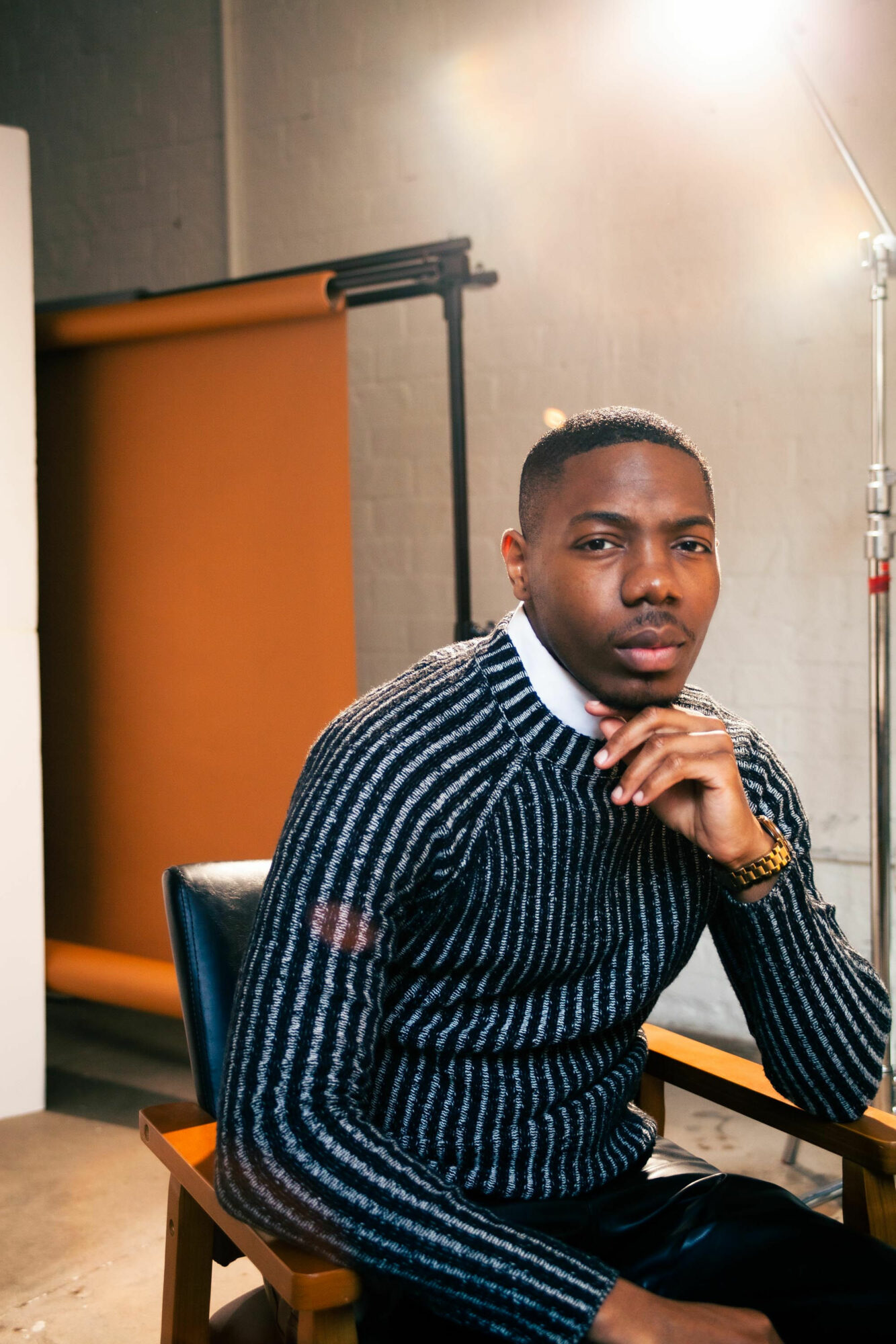 Man with short hair and a striped sweater sitting at a table, looking at the camera, in a studio setting.