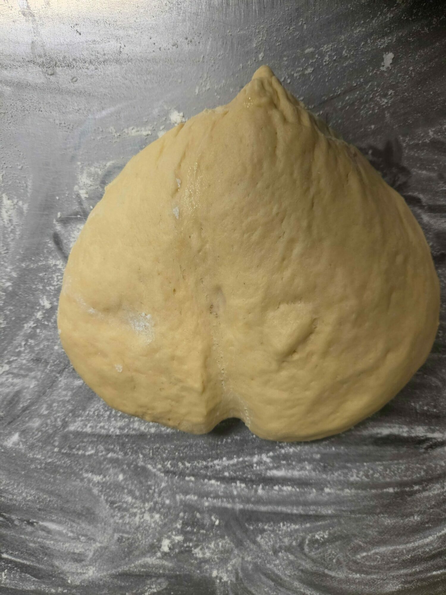 Dough ball on a floured surface, ready for baking, with a slightly irregular shape and smooth texture.