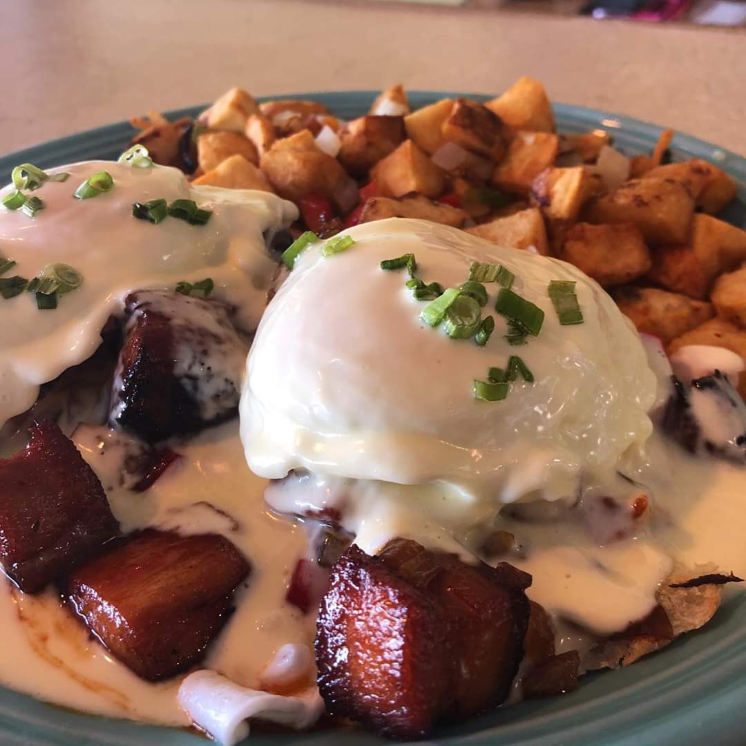 Two poached eggs with green herbs on a plate with roasted potatoes and crispy bacon pieces.