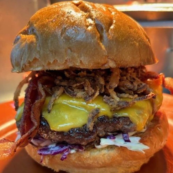 Close-up of a burger with beef patty, melted cheese, bacon, shredded lettuce, and a bun, viewed from the front.