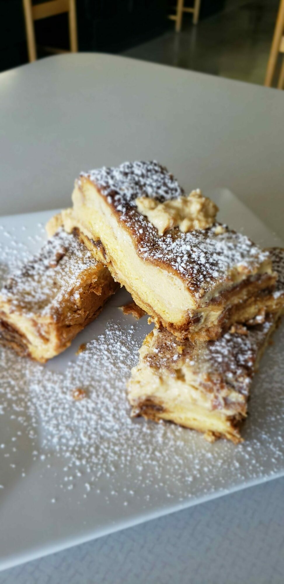 Piece of cake with powdered sugar on top, showing layers of cream and cake, on a white plate.
