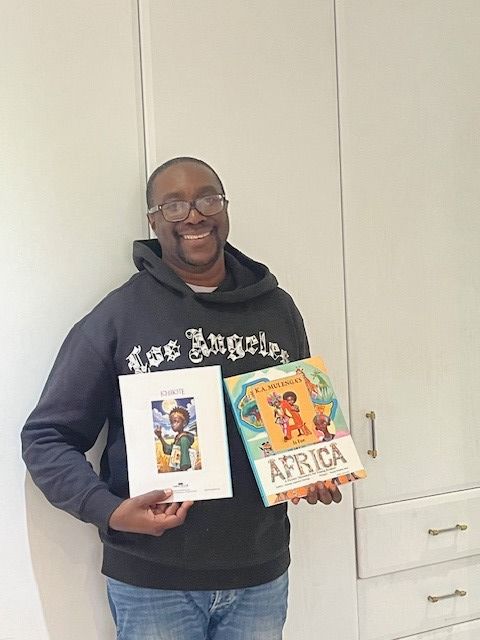Person holding two colorful books, standing against a plain white wall, wearing glasses and a black hoodie.
