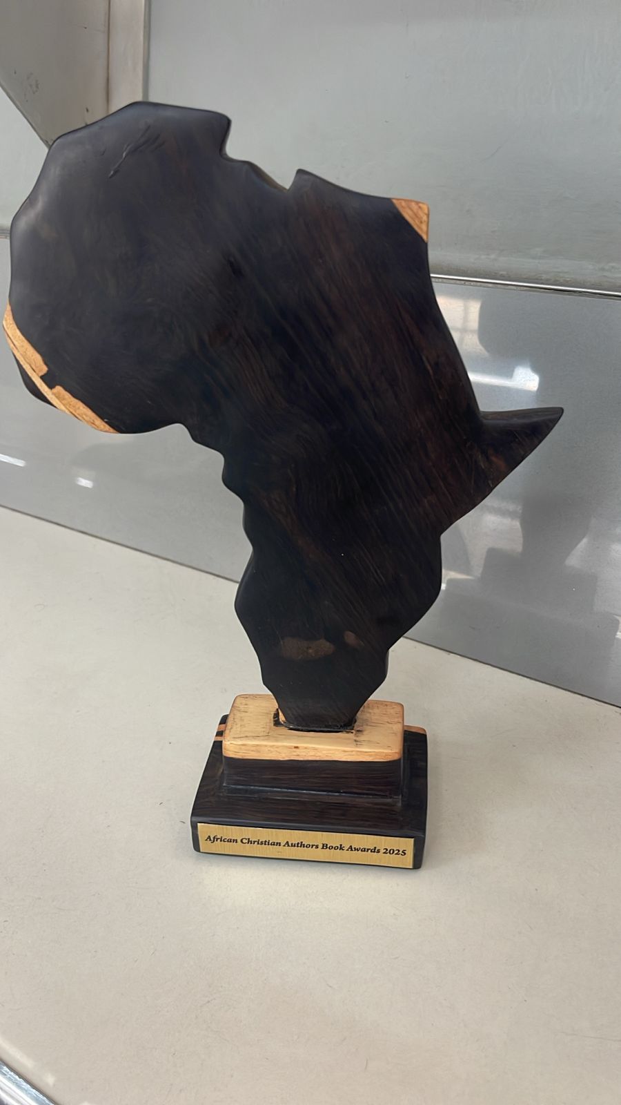 Black sculpture of the African continent on a wooden base with a plaque, placed on a white surface.
